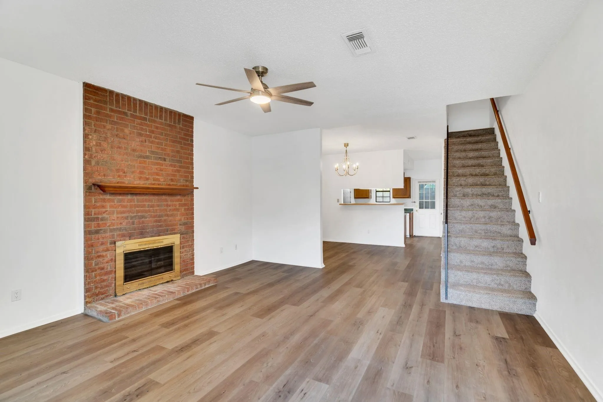 Brick-faced fireplace with a wood mantel, wood-finish flooring, and a ceiling fan