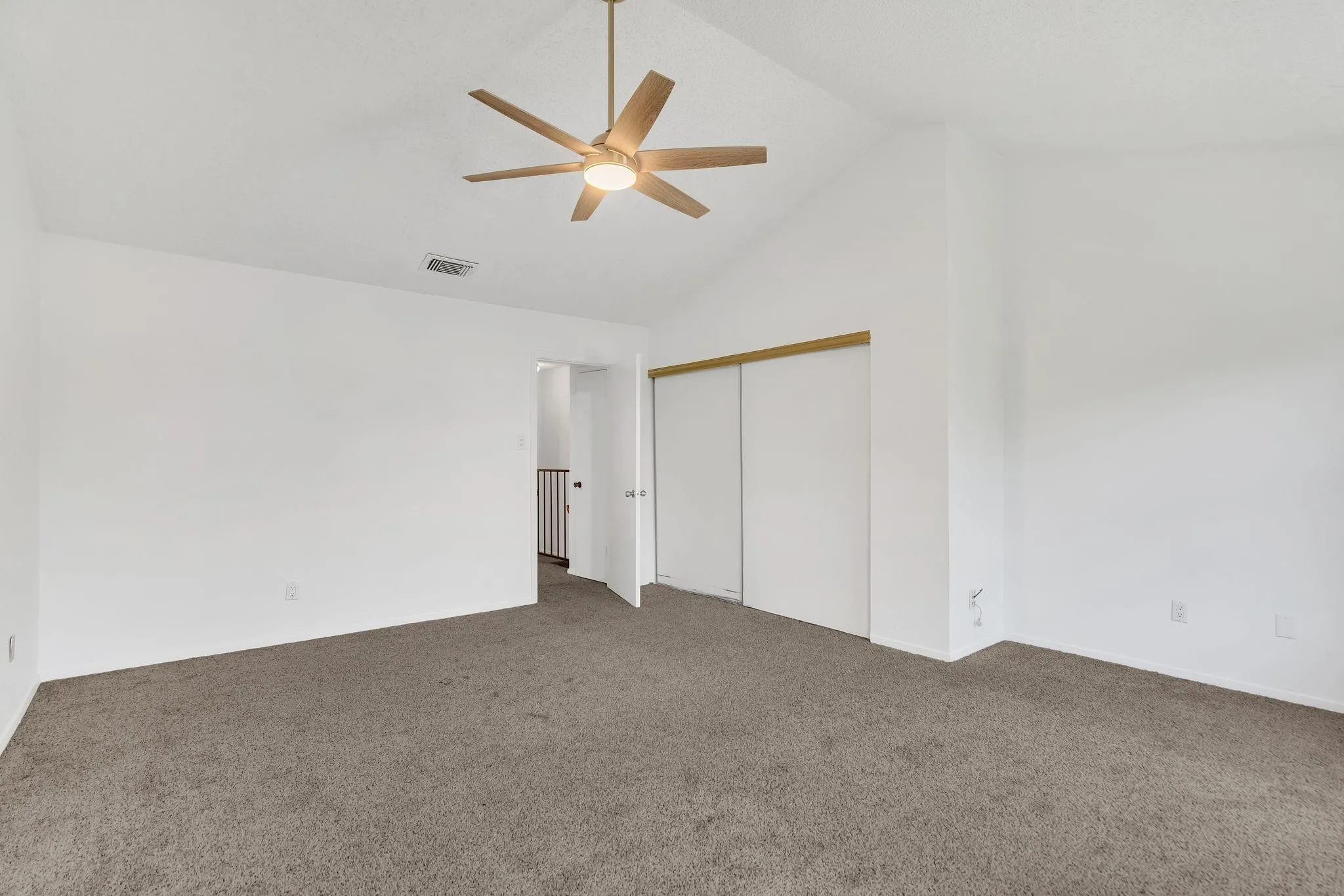 Vaulted ceiling, ceiling fan with integrated lighting, carpeted flooring, sliding closet doors, and neutral wall tones