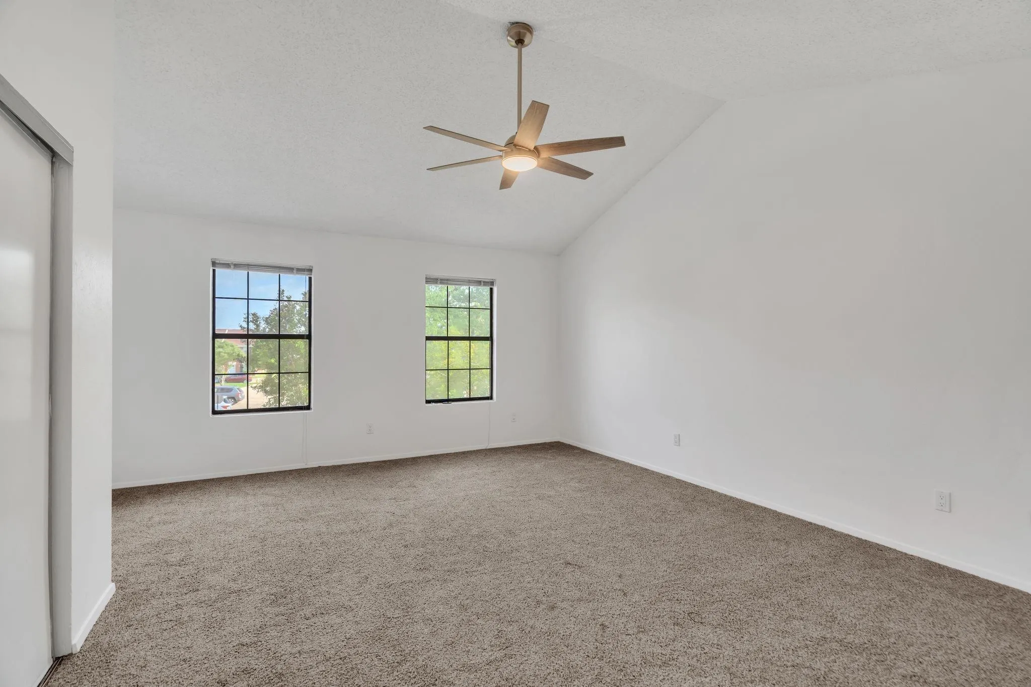 Vaulted ceiling with a ceiling fan and integrated lighting, two double-hung windows, wall-to-wall carpeting, and a built-in closet with sliding doors