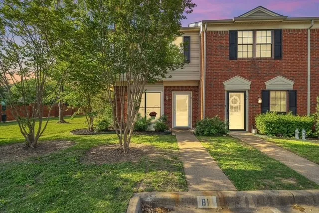 Brick facade with accent siding, individual entryways, mature trees, and a concrete paver walkway