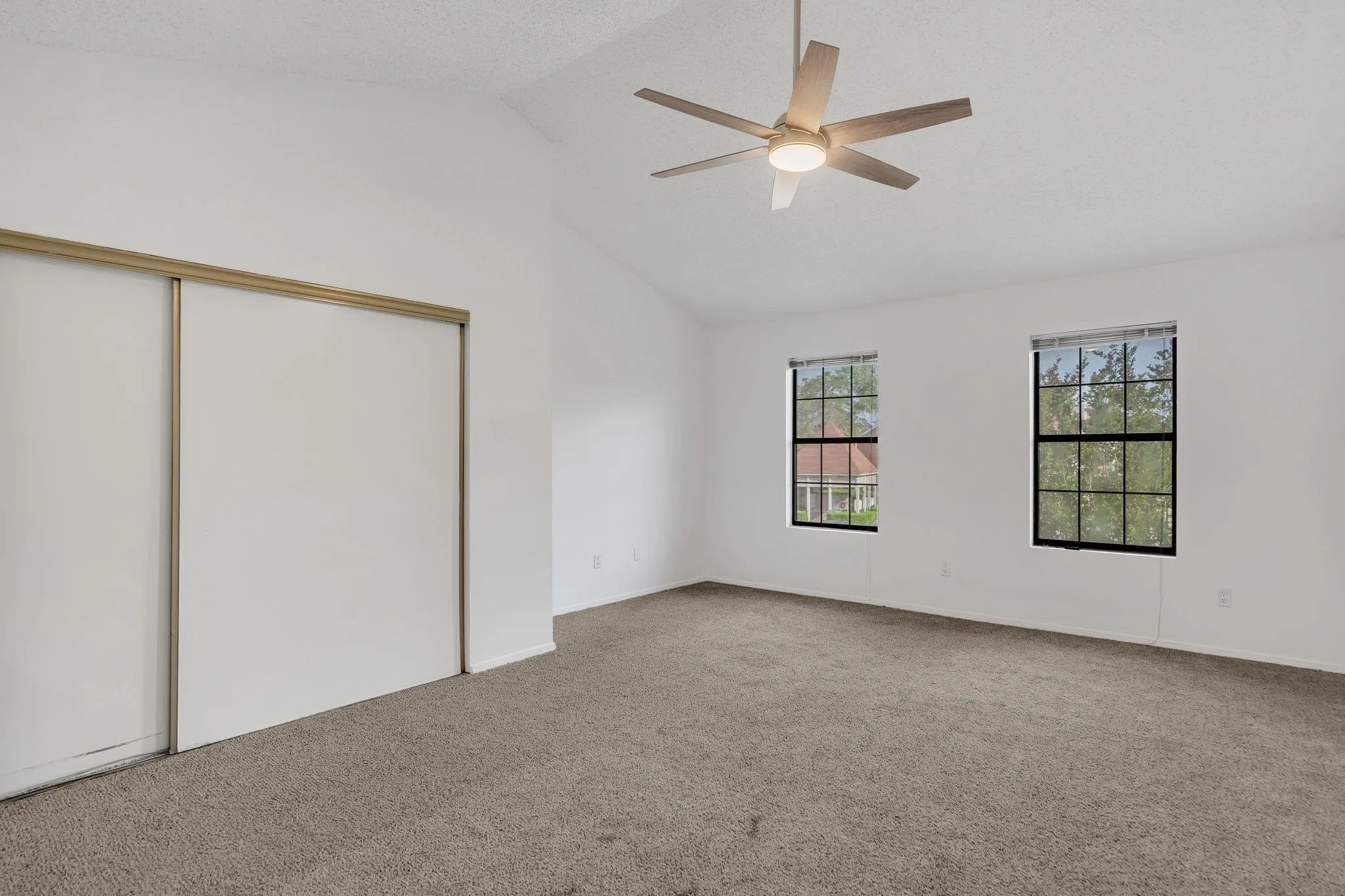 Vaulted ceiling with a ceiling fan, two windows, carpet flooring, and sliding closet doors