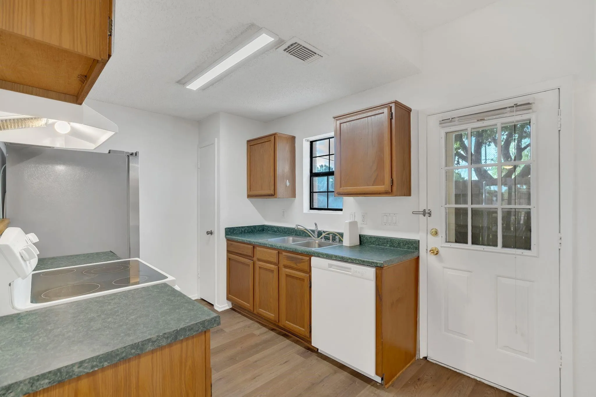 Kitchen featuring wood-finish cabinetry, a stainless steel refrigerator, a built-in dishwasher, and a glass-paneled exterior door