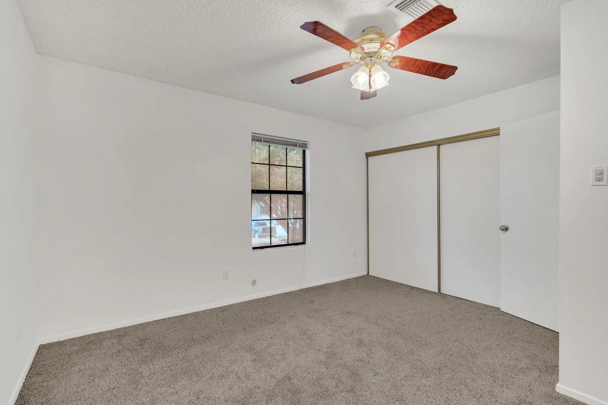 Room featuring a window, ceiling fan with light fixture, carpeted flooring, and sliding closet doors