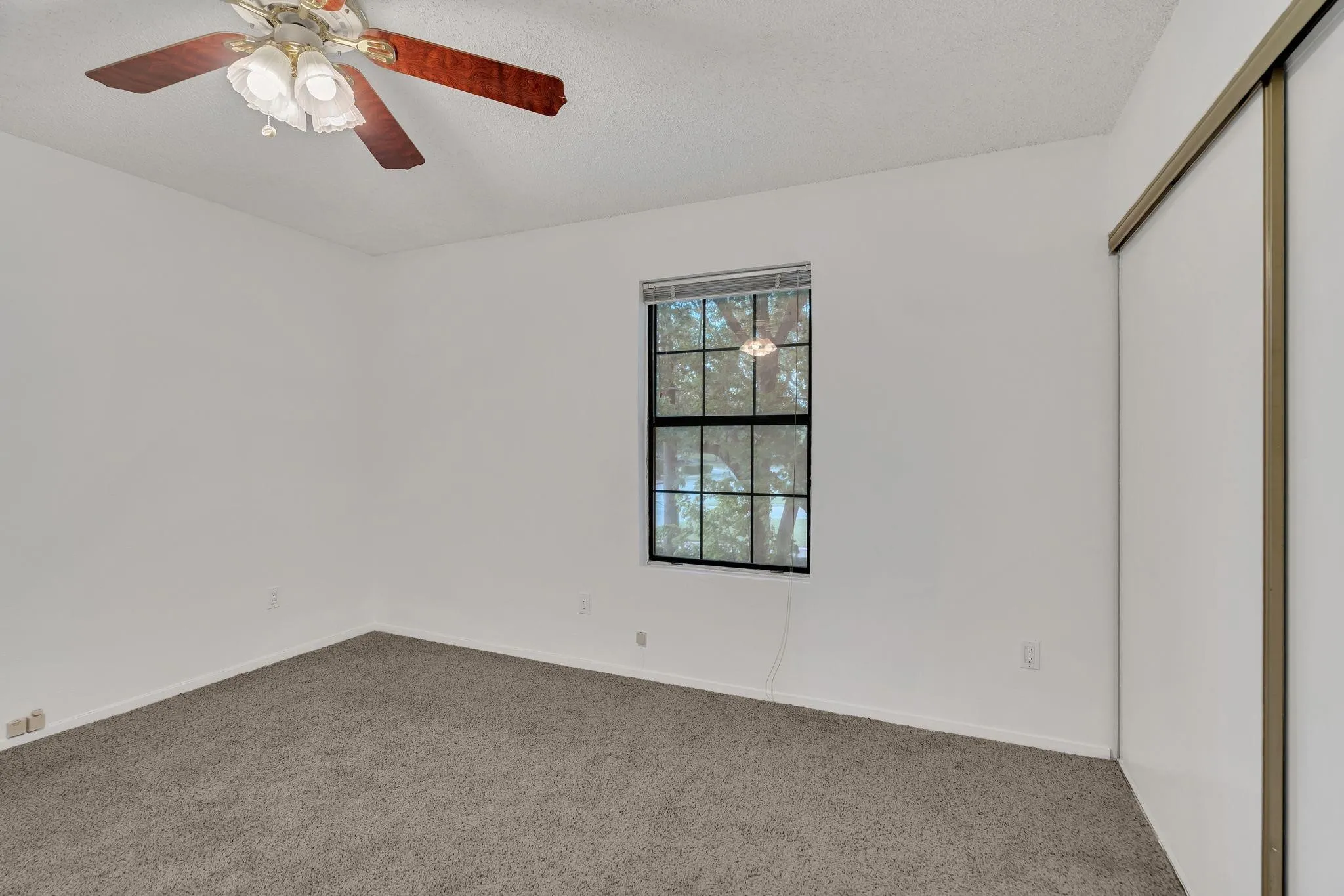 Recessed window with black gridded panes, ceiling fan with integrated lighting, textured ceiling, and sliding closet doors