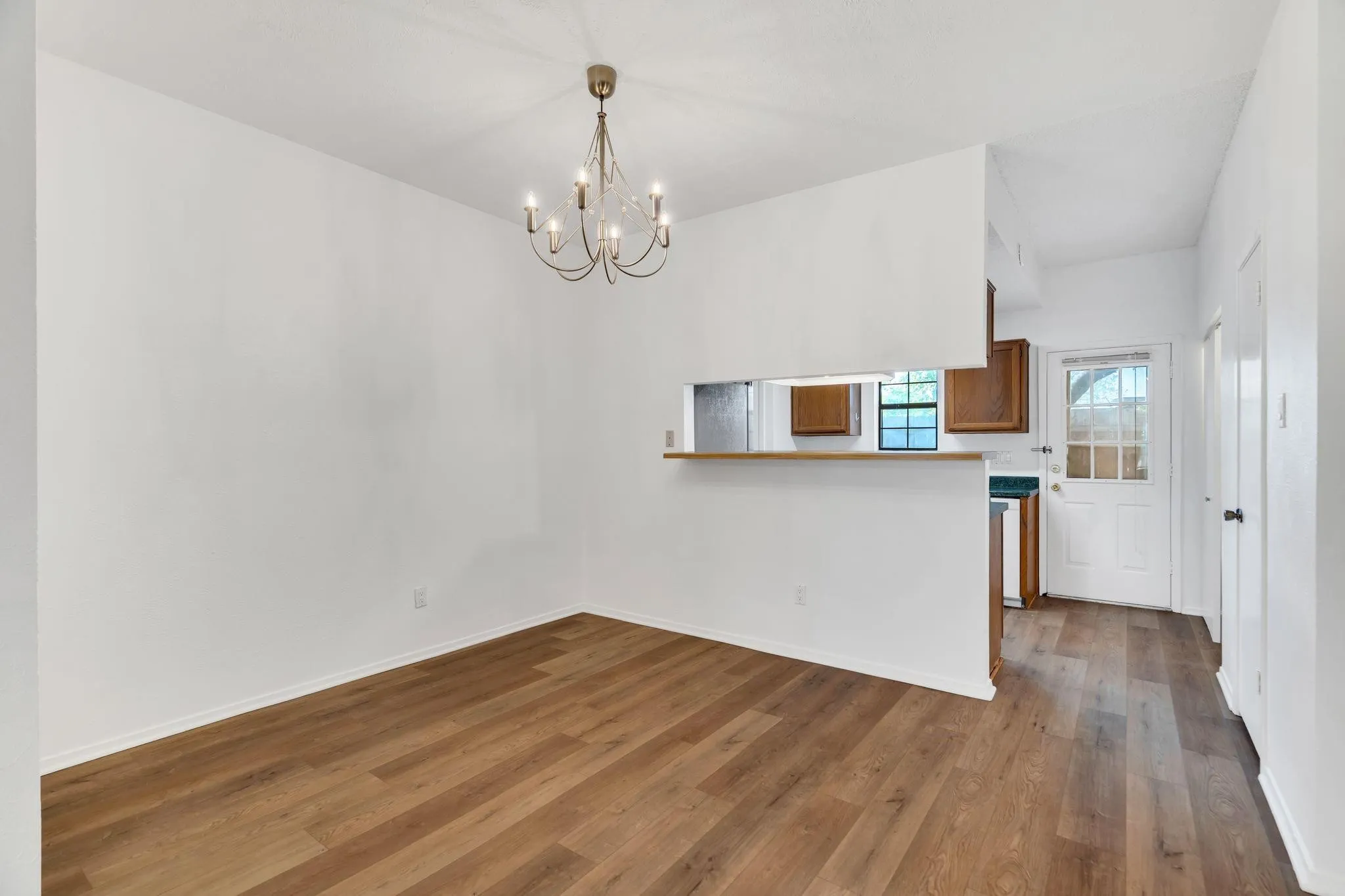 Wood-finish flooring, overhead chandelier, white walls, passthrough counter, and a paneled door