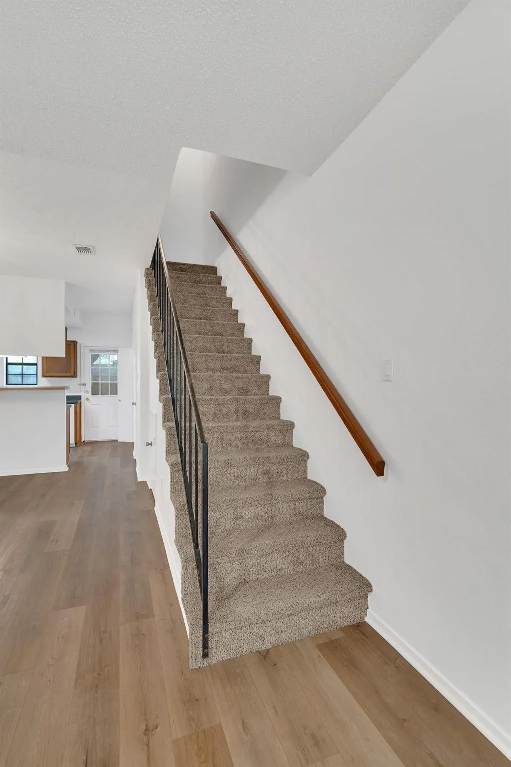 Carpeted staircase with a wood handrail, black metal balusters, and wood-finish flooring