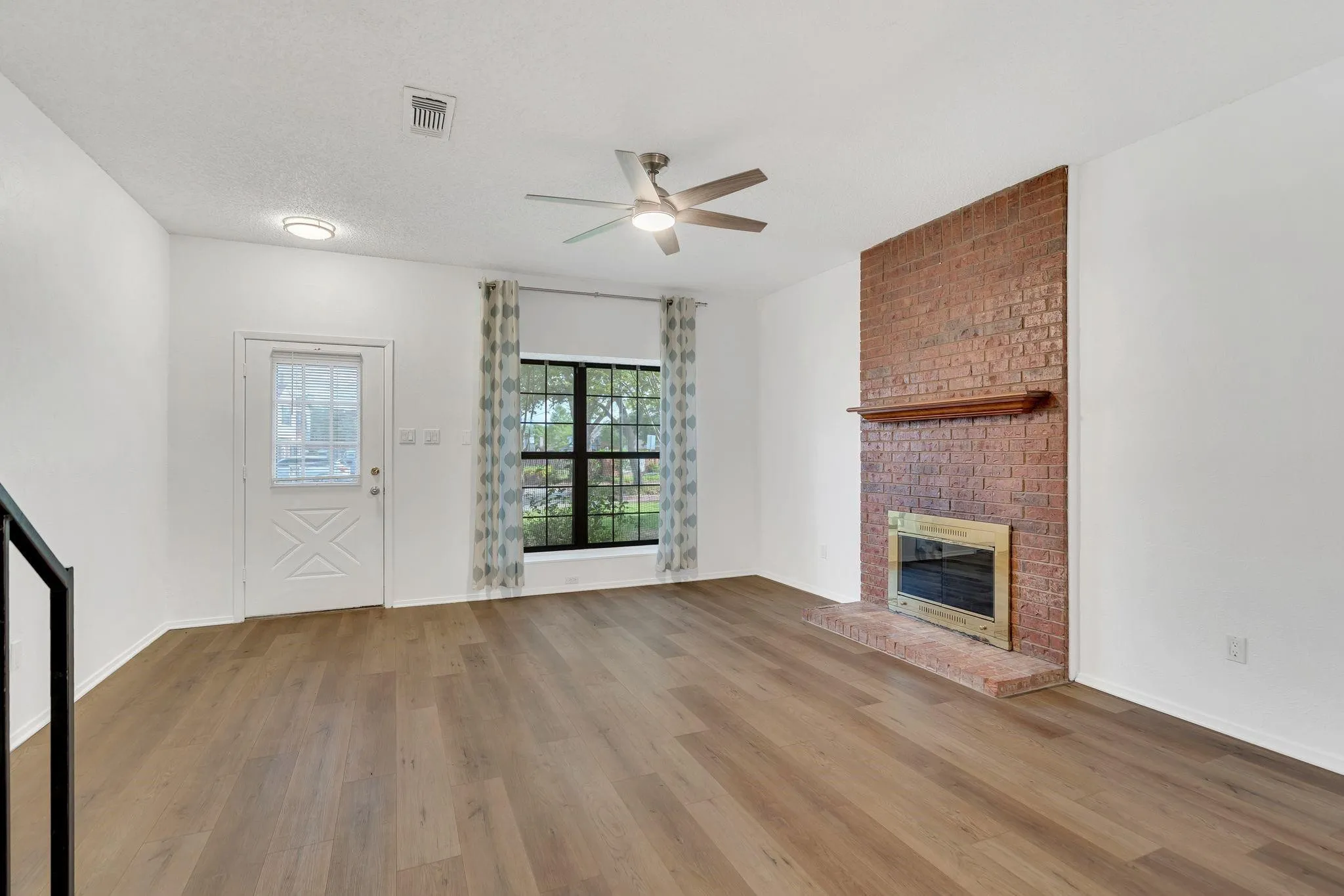 Wood-finish flooring throughout, brick fireplace with a wood mantel, ceiling fan, and a transom-style door