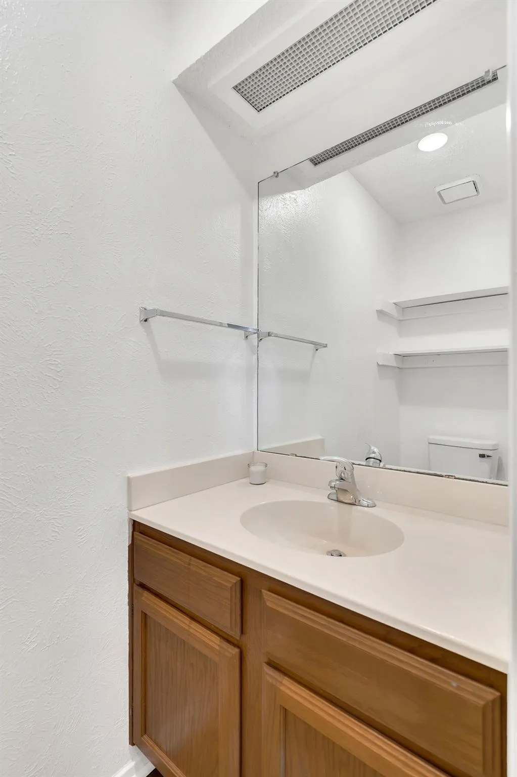 Vanity with wood-finish cabinetry, integrated sink, and light-toned countertop