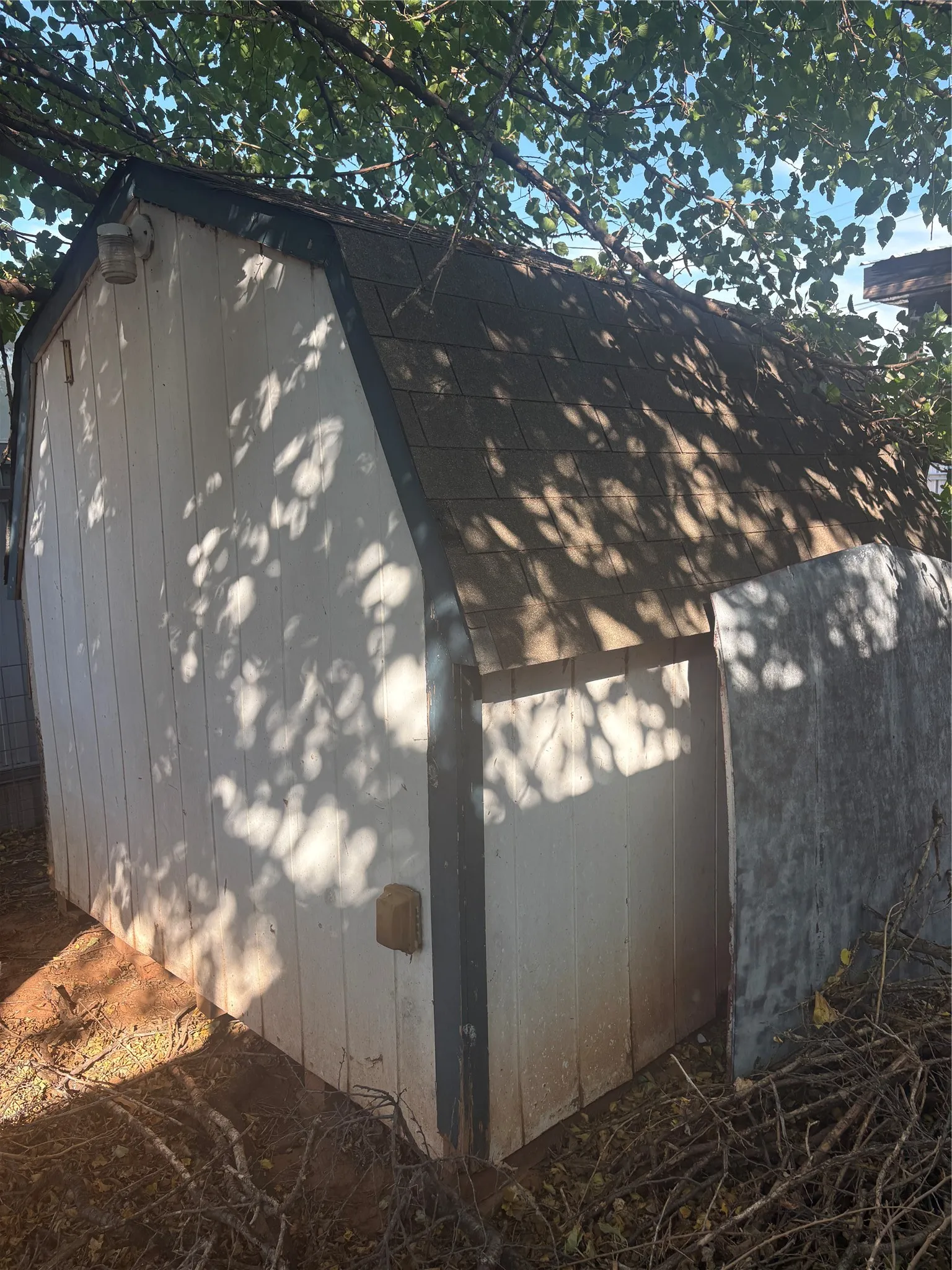 White-painted wood siding structure with a gambrel roof and asphalt shingles