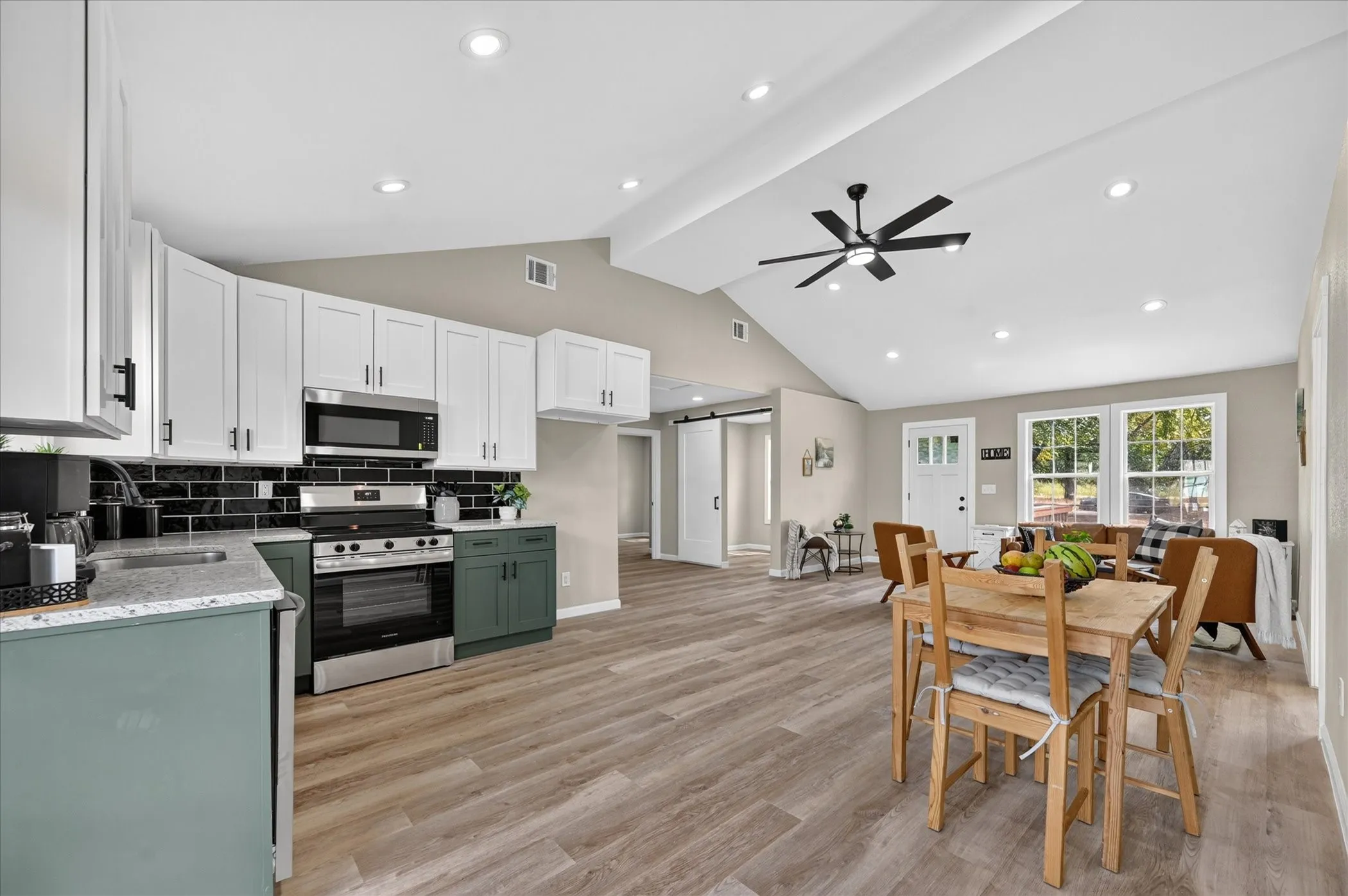 Vaulted ceiling with recessed lighting and ceiling fan, wood-finish flooring, and a kitchen featuring stainless steel appliances, two-tone cabinetry, and a subway tile backsplash