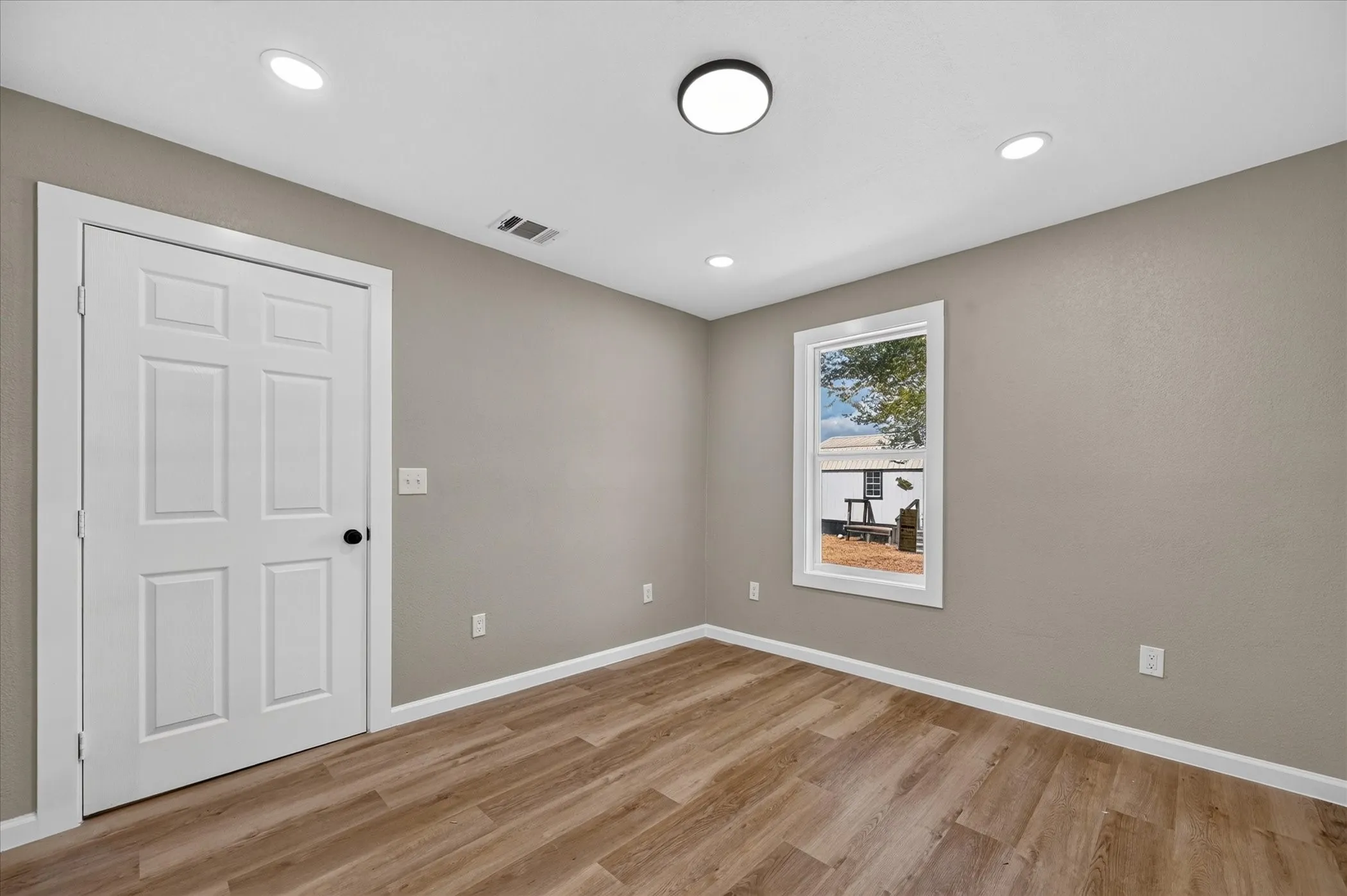 Wood-finish flooring, recessed ceiling lights, neutral wall paint, white trim, and a white six-panel door