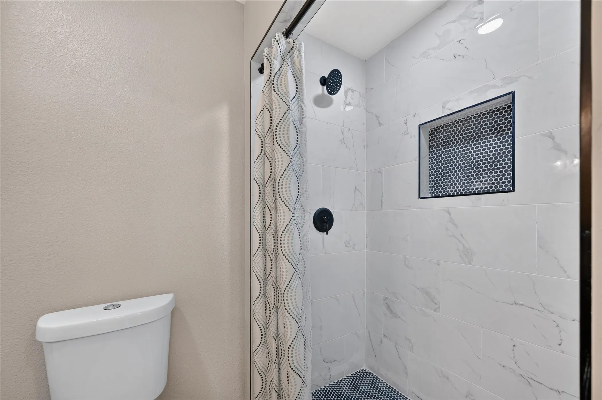 Bathroom #3 Shower featuring large format white tile walls with veining, a recessed niche with penny tile, and a black penny tile floor