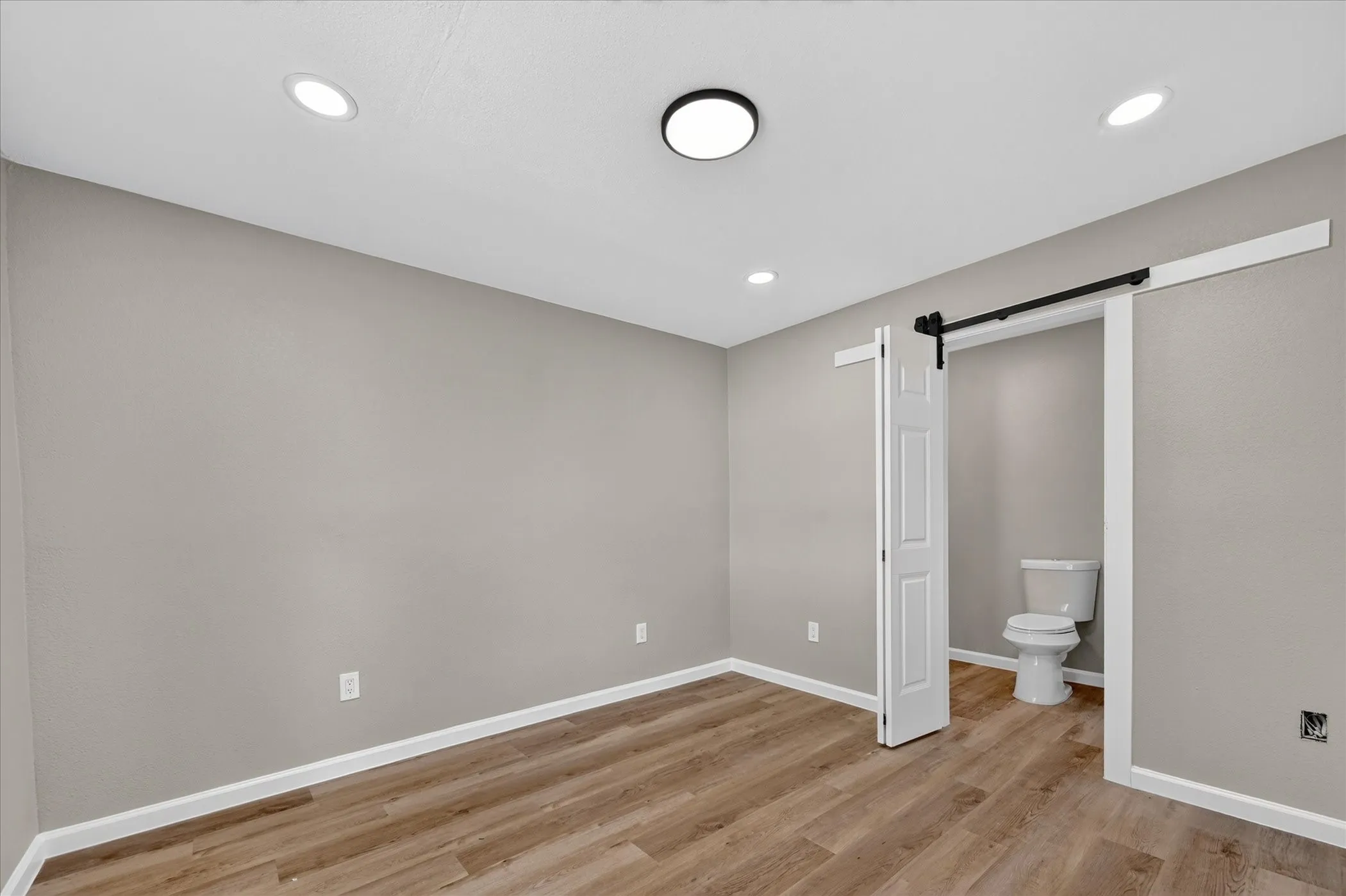 Recessed ceiling lighting, wood-finish flooring, and a barn door entry to a private water closet