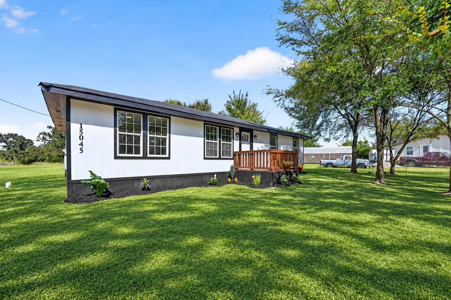 White siding exterior with black trim, wood deck, multiple windows, and a black shingle roof. Grass is AI.