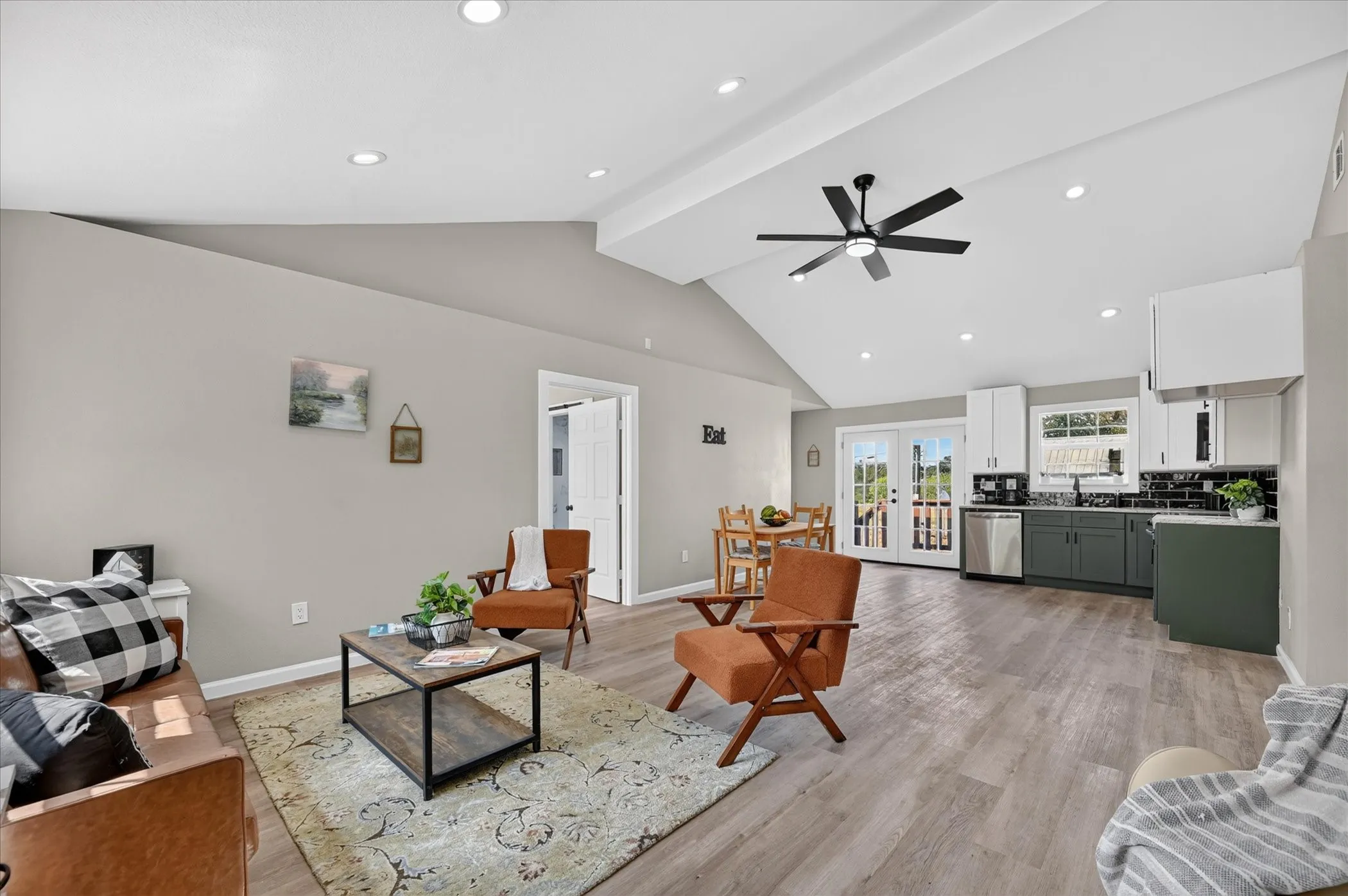 Vaulted ceiling with recessed lighting and ceiling fan, wood-finish flooring, white double French doors, two-tone kitchen cabinetry, and a black subway tile backsplash