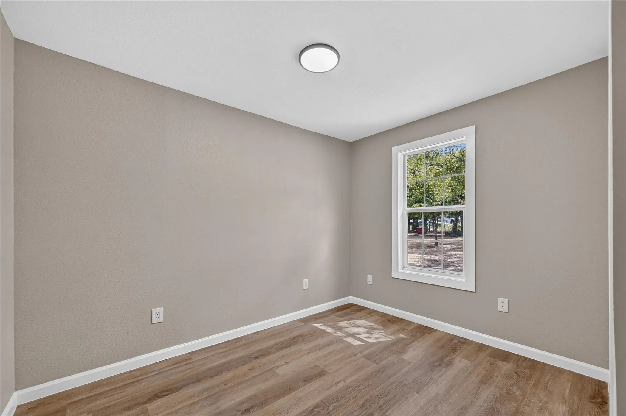 Neutral wall color, wood-finish flooring, white trim, and a window with white casing