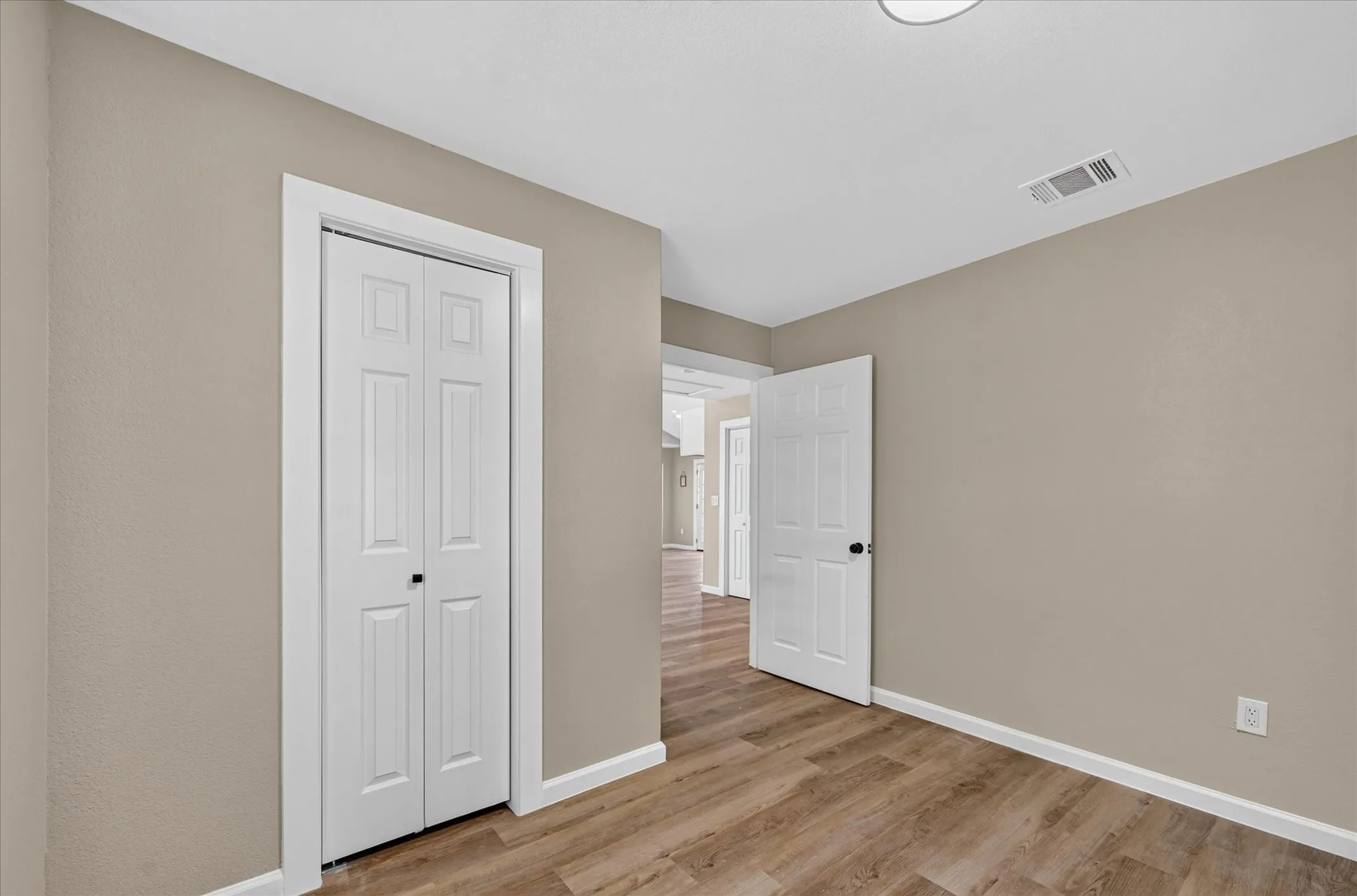 Wood-finish flooring, neutral wall tones, bi-fold closet doors, and white trim