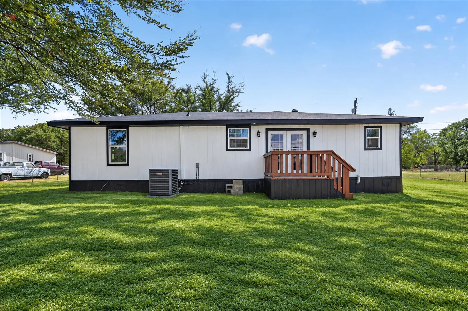 Grass is AI. White siding with dark trim, dual exterior light fixtures, a brown wood-finish deck with railings, and a double-door entry