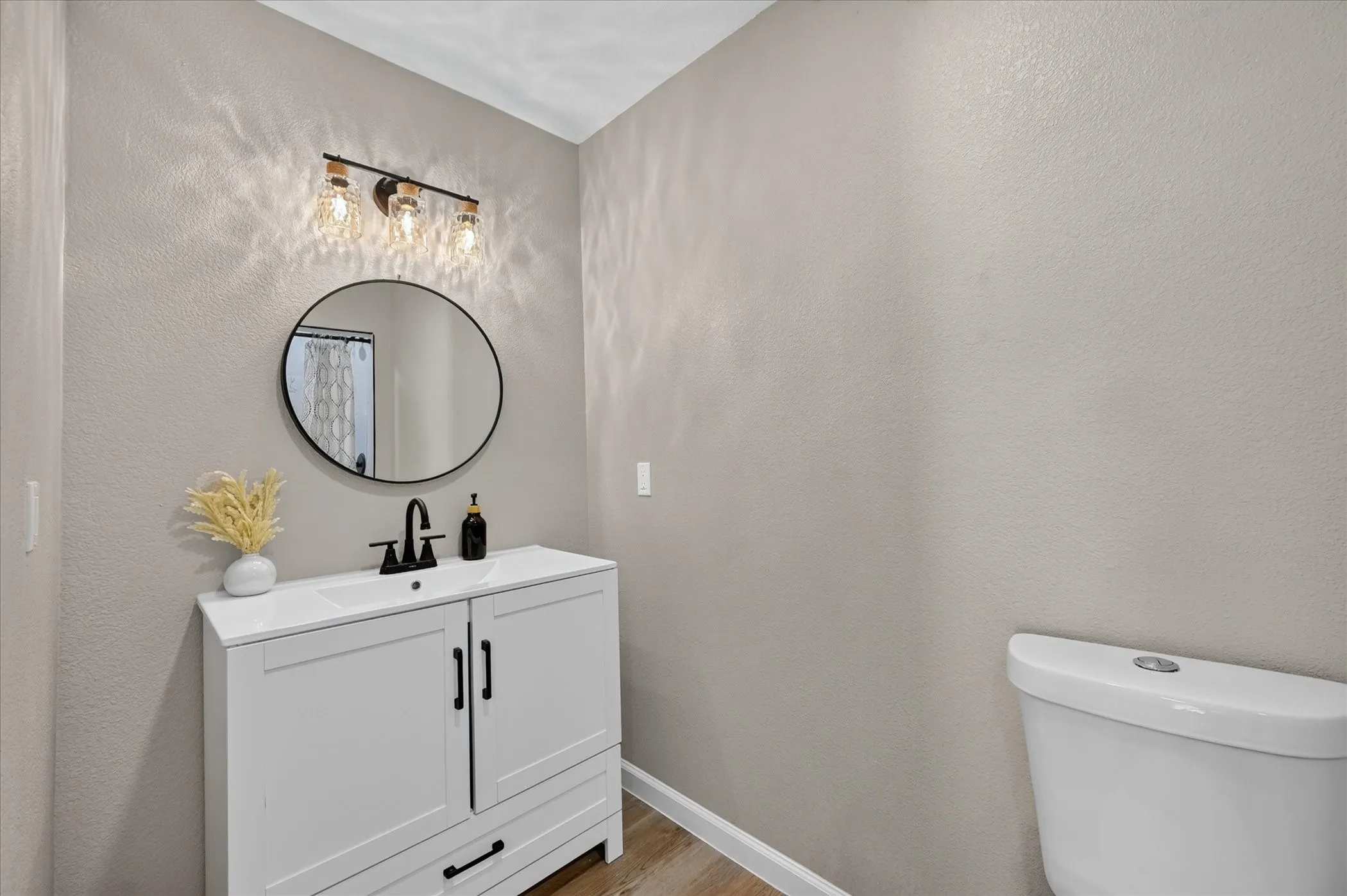 Bathroom #3.  White vanity with an integrated sink, matte black faucet, round framed mirror, and three-light vanity fixture