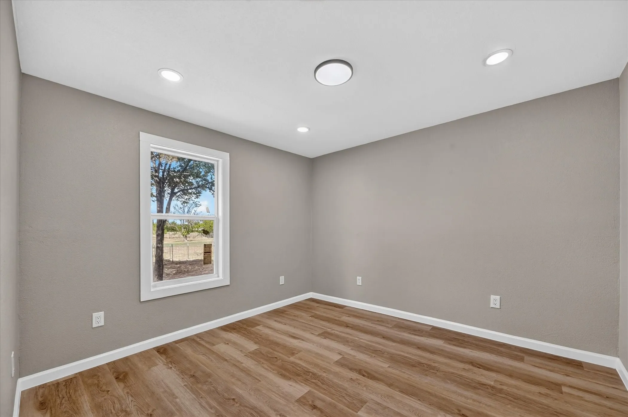 Wood-finish flooring, neutral wall tones, white trim, recessed lighting, and a window with outdoor scenery