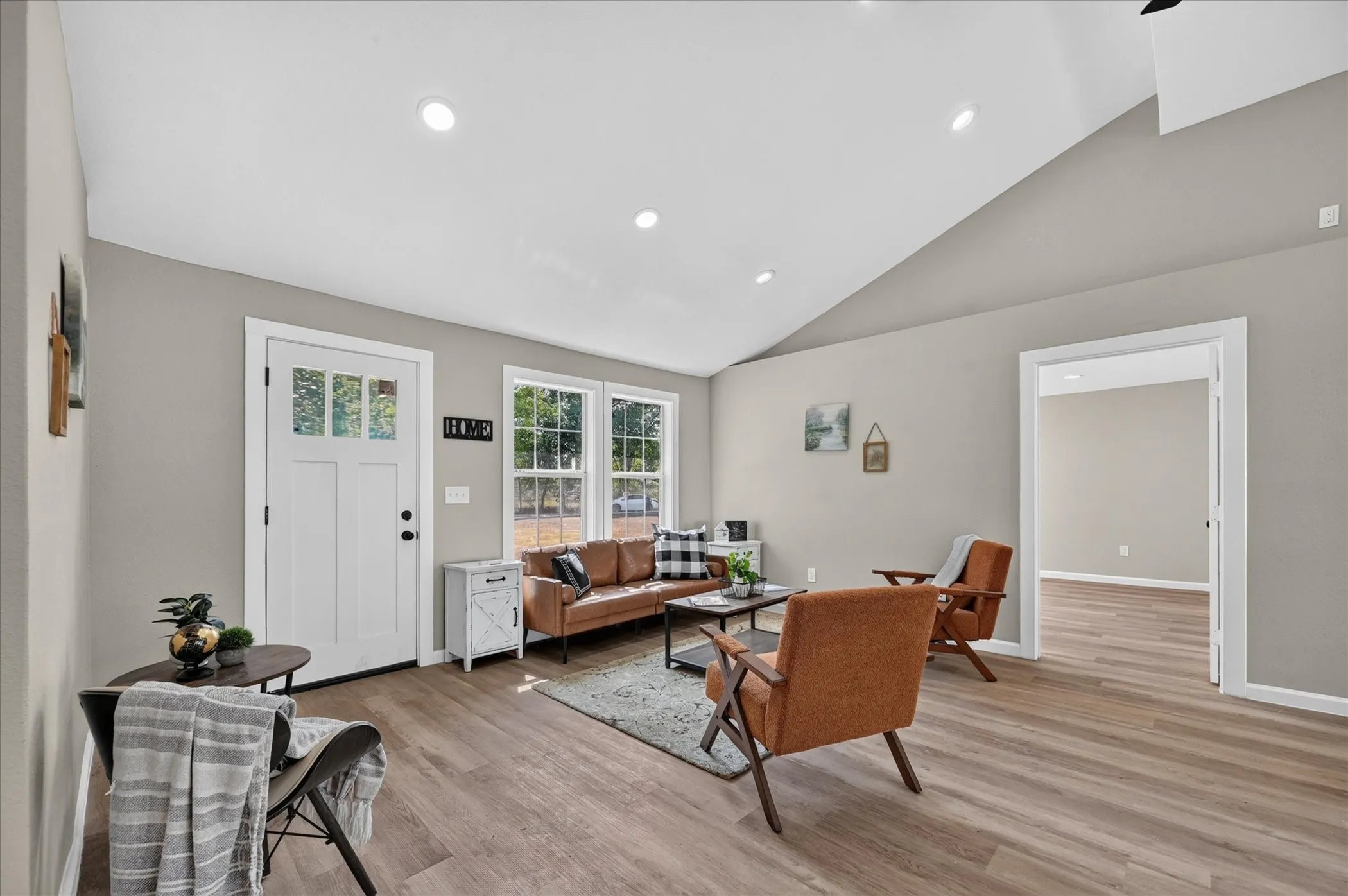 Vaulted ceiling with recessed lighting, wood-finish flooring, white paneled entry door with glass inserts, and multiple windows