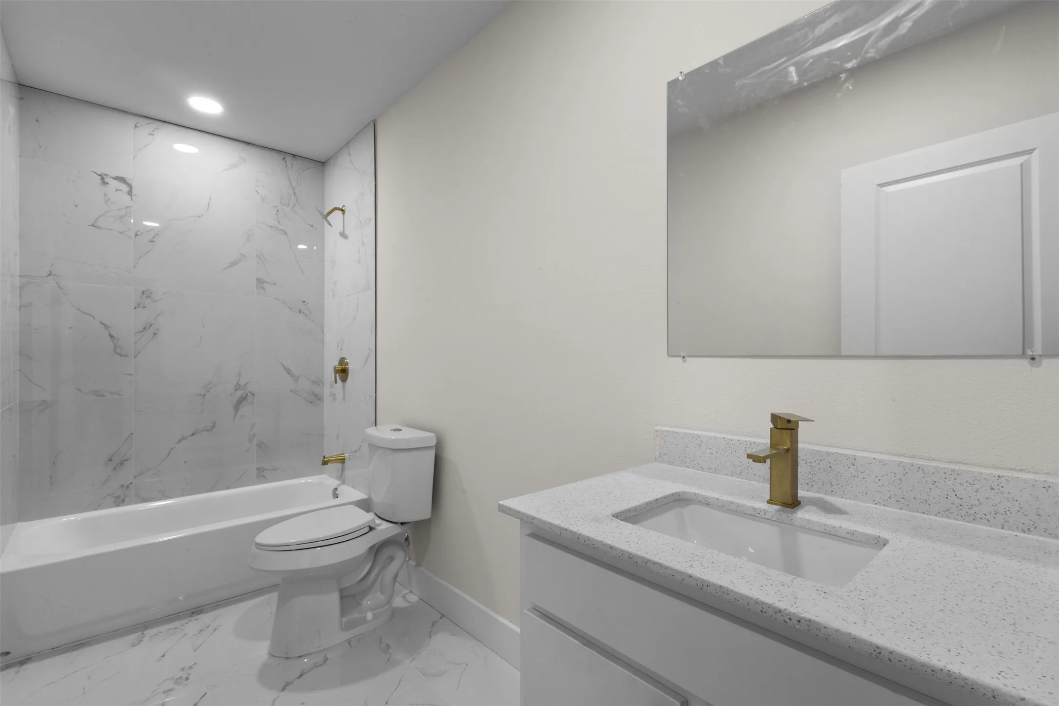 Integrated bathtub with marble-look tile surround, recessed lighting, and a white vanity with a light speckled countertop