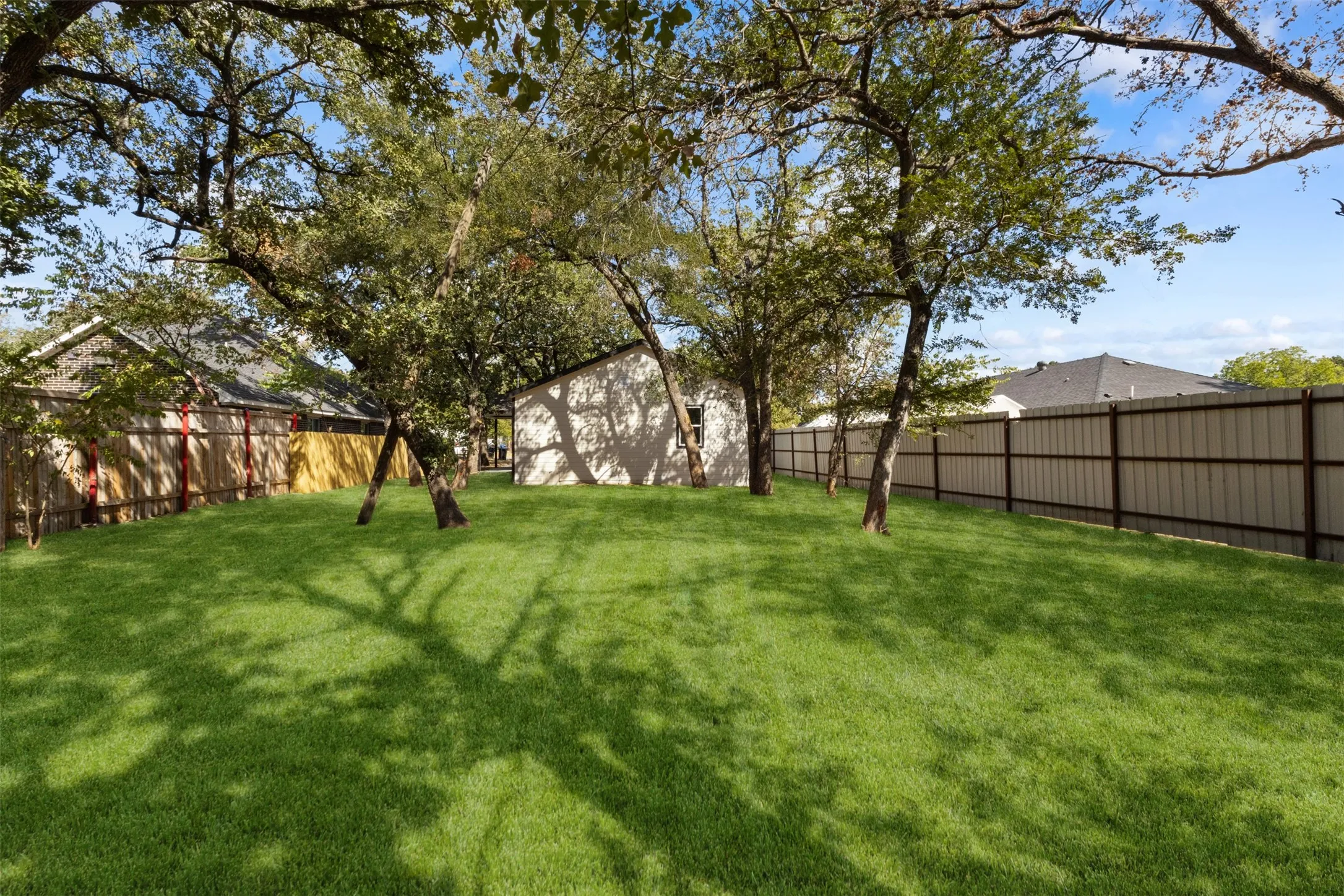 Expansive backyard with a lush lawn, mature trees, and a combination of wood and metal fencing