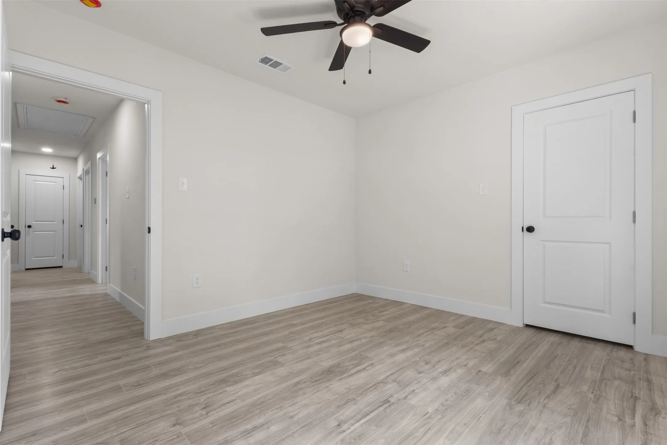 Light wood-finish flooring, neutral wall tones, white trim, a ceiling fan with integrated lighting, and a paneled interior door