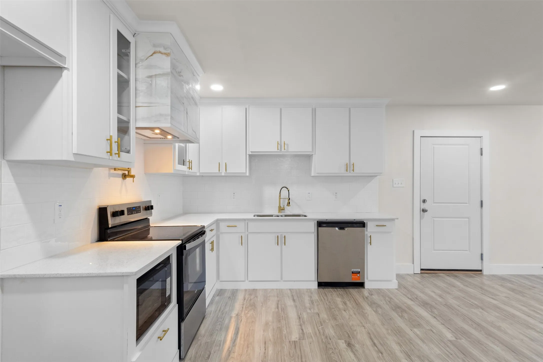 Modern kitchen featuring white cabinetry with gold-finish hardware, stainless steel appliances, light-toned countertops, and wood-finish flooring