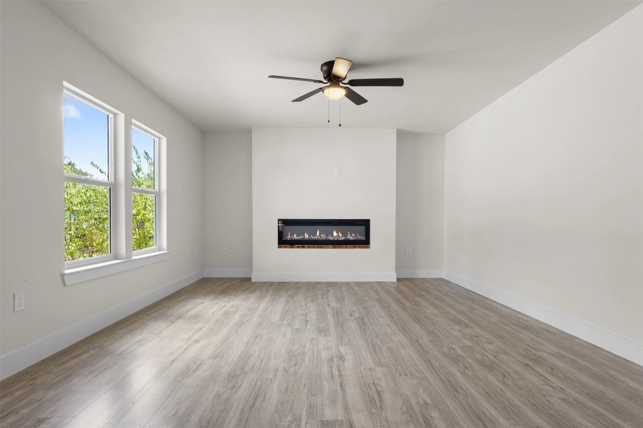 Bright interior with wood-finish flooring, a contemporary electric fireplace, dual windows, and a ceiling fan