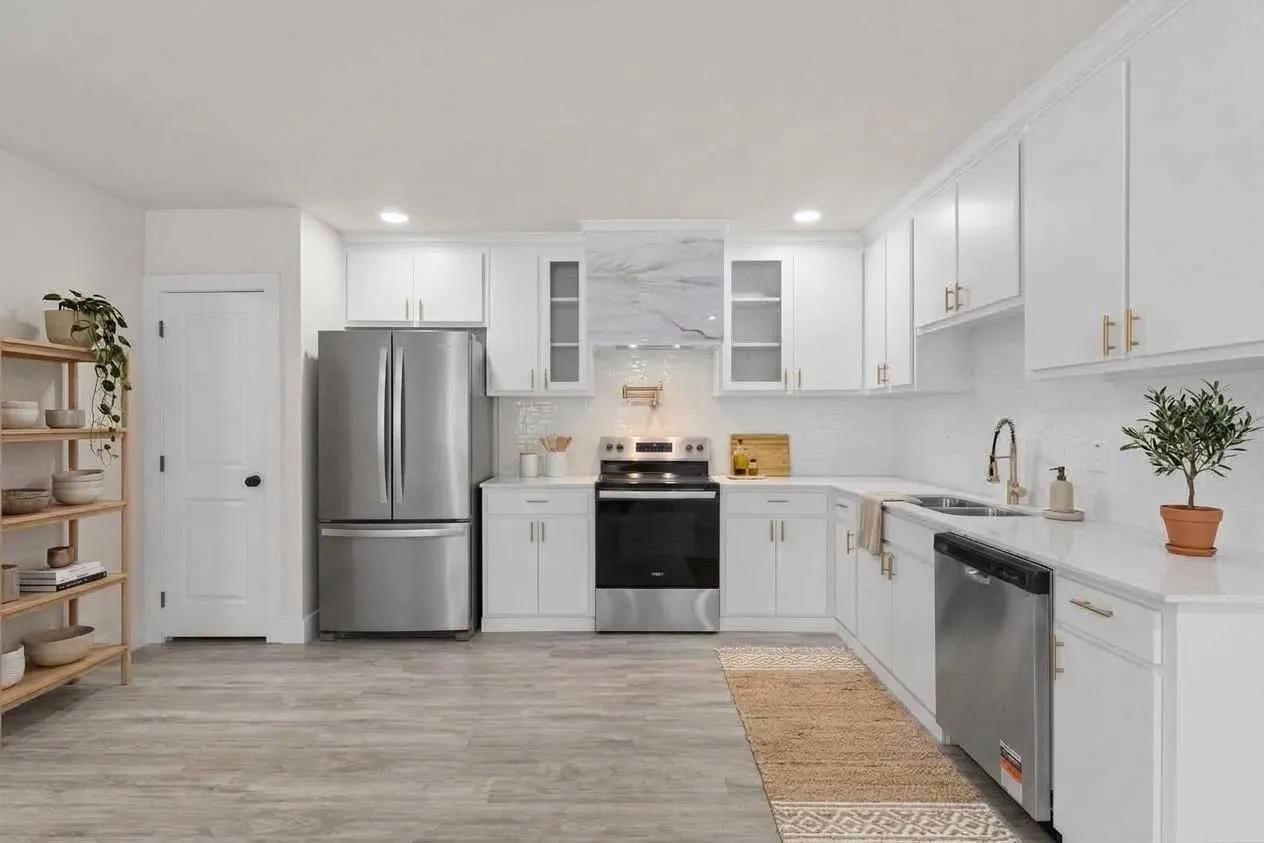Modern kitchen featuring white cabinetry with gold-finish hardware, stainless steel appliances, light-toned countertops, and wood-finish flooring