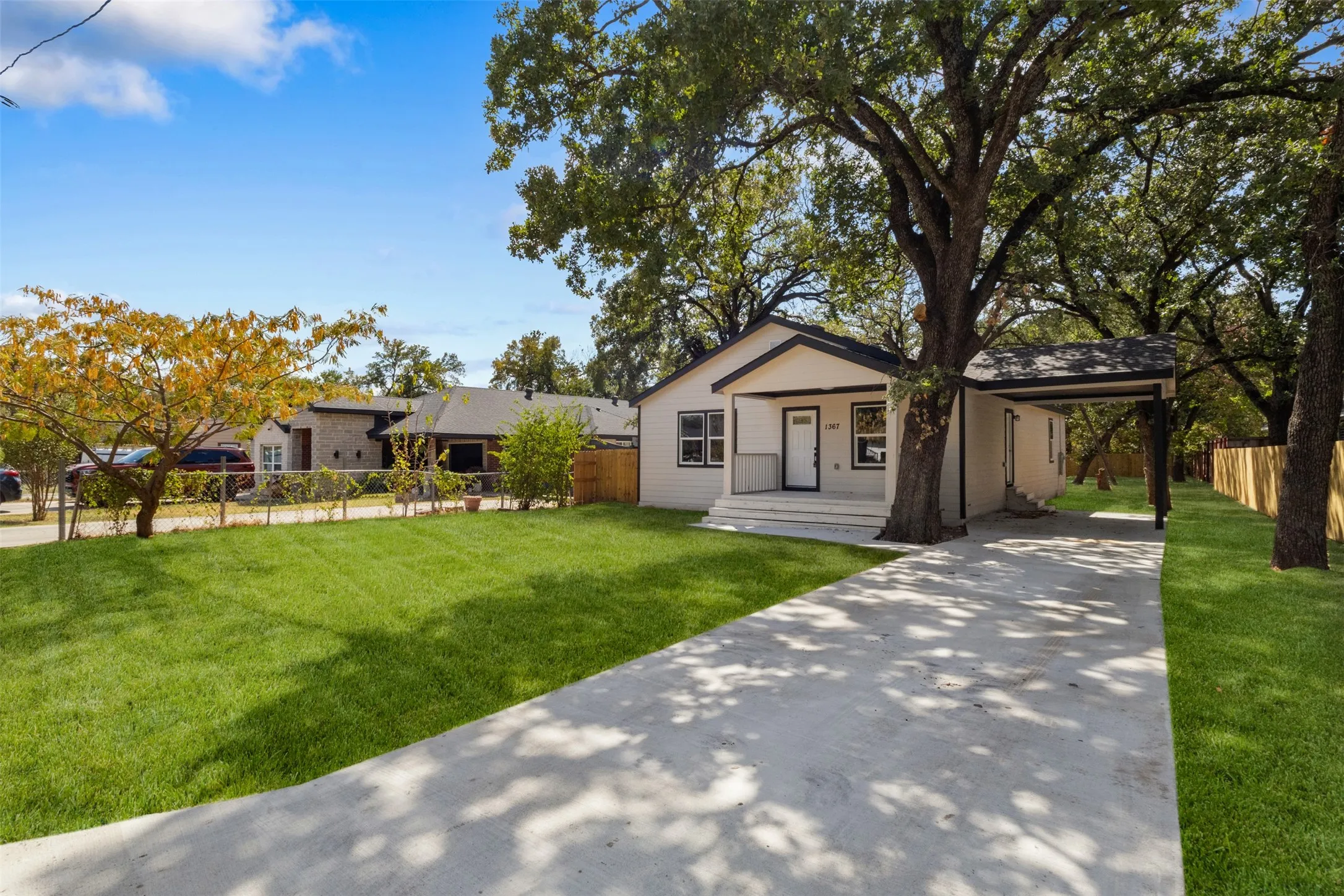 White siding exterior with black trim, concrete driveway, covered carport, front porch with steps, and mature trees