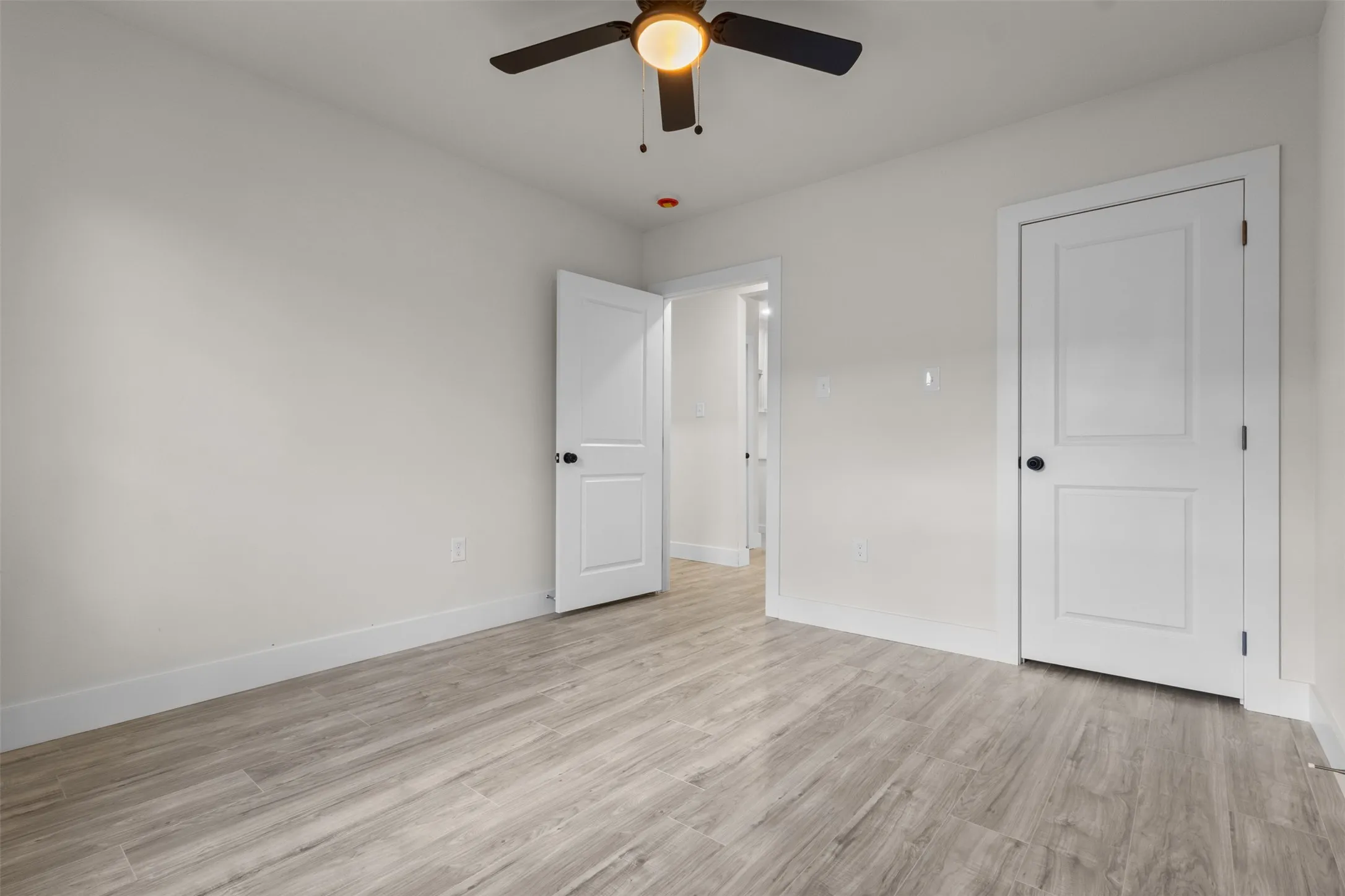 Neutral wall color, wood-finish flooring, ceiling fan with integrated lighting, and white paneled doors