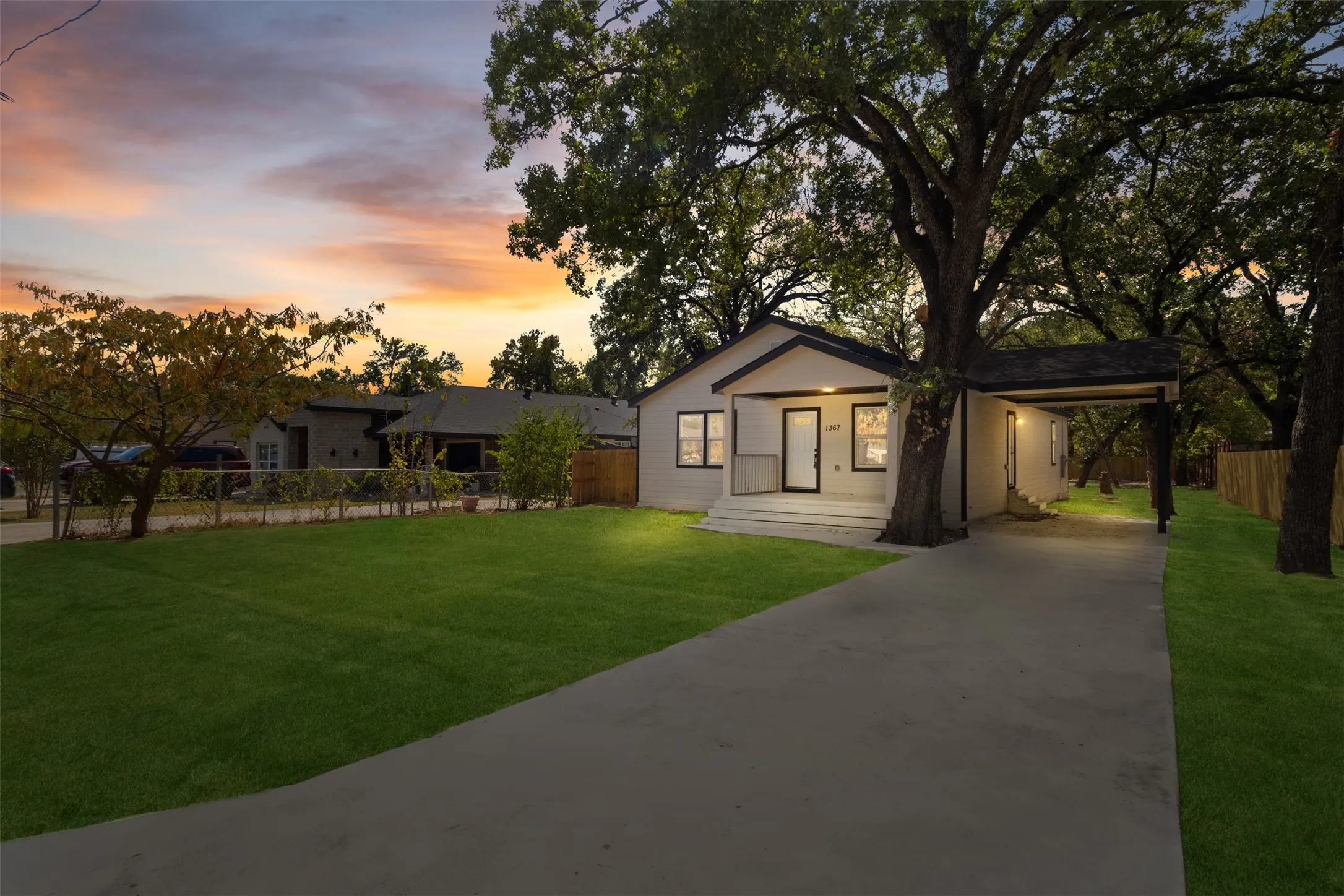 Exterior featuring a covered porch, attached carport, mature trees, concrete driveway, and manicured lawn