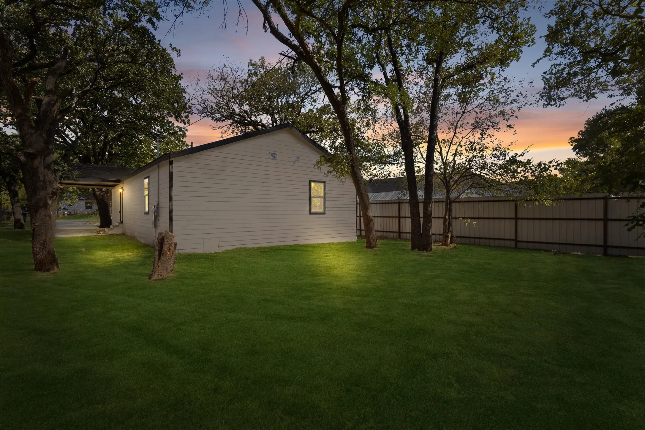 Expansive green lawn with mature trees and a privacy fence