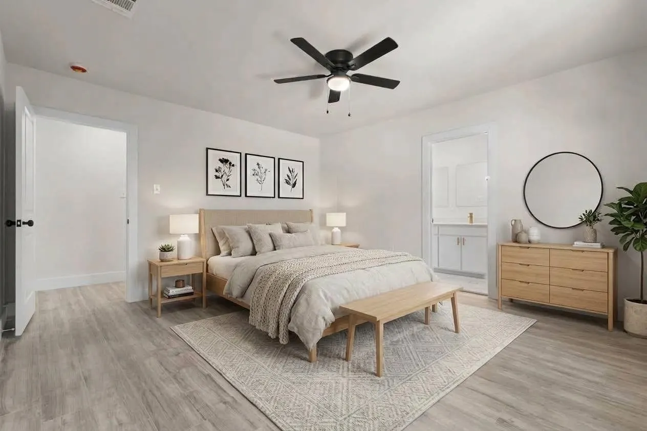 Wood-finish flooring, ceiling fan with integrated lighting, door with black hardware, and an open doorway revealing a bathroom vanity