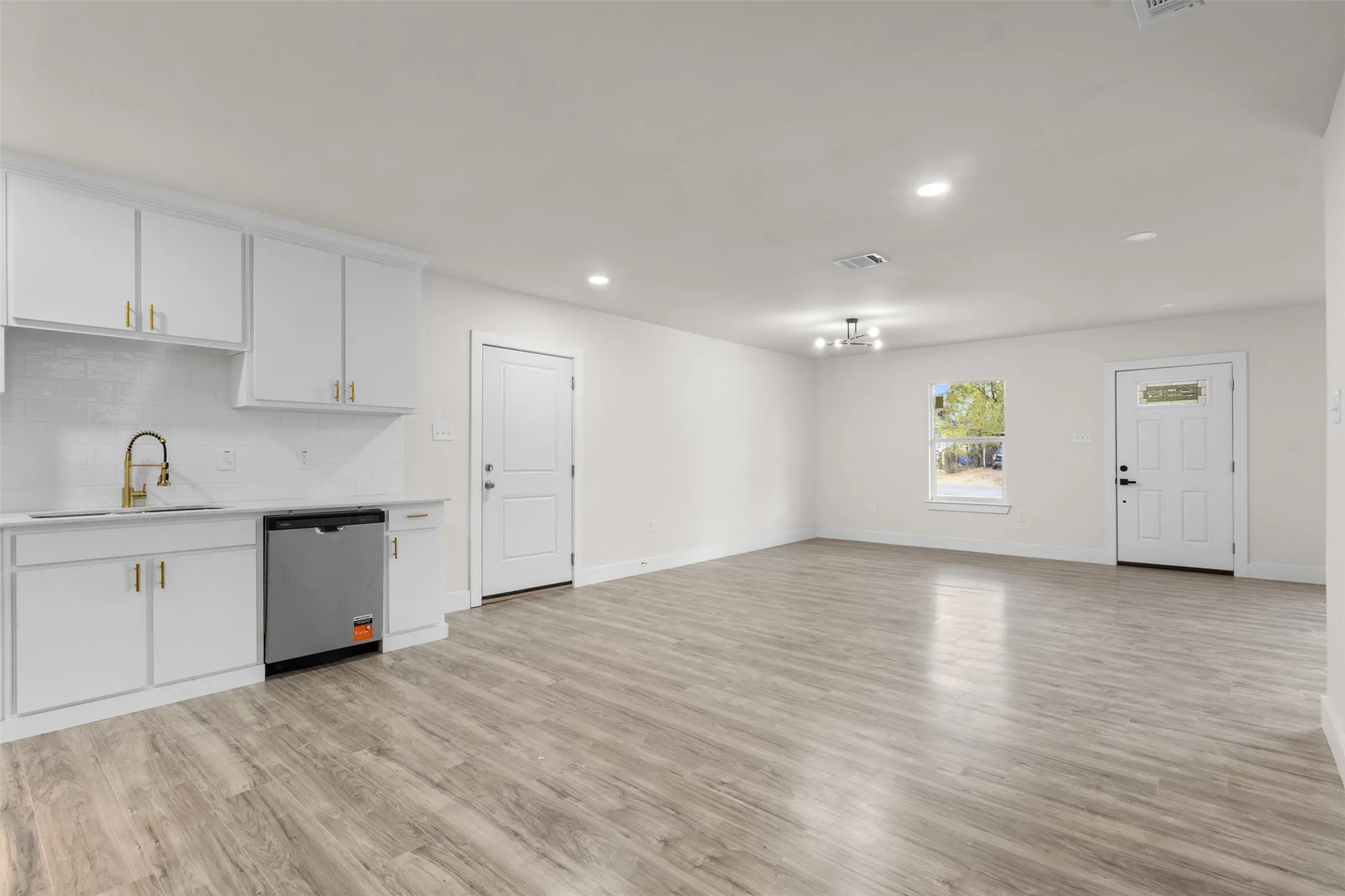 Wood-finish flooring throughout, white cabinetry with gold-tone hardware, stainless steel dishwasher, white subway tile backsplash, and recessed lighting