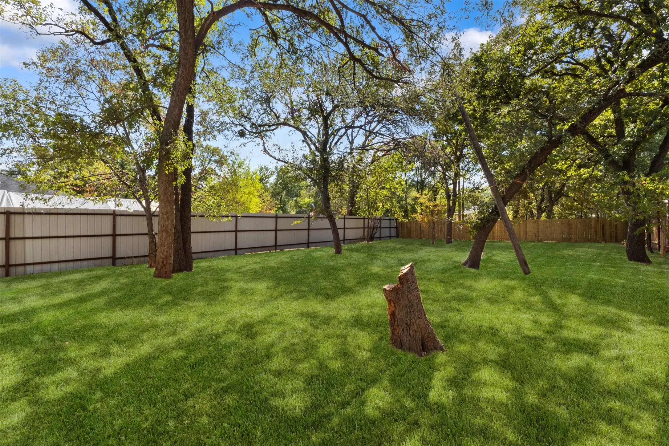 Spacious backyard featuring a manicured lawn, mature trees, and a privacy fence
