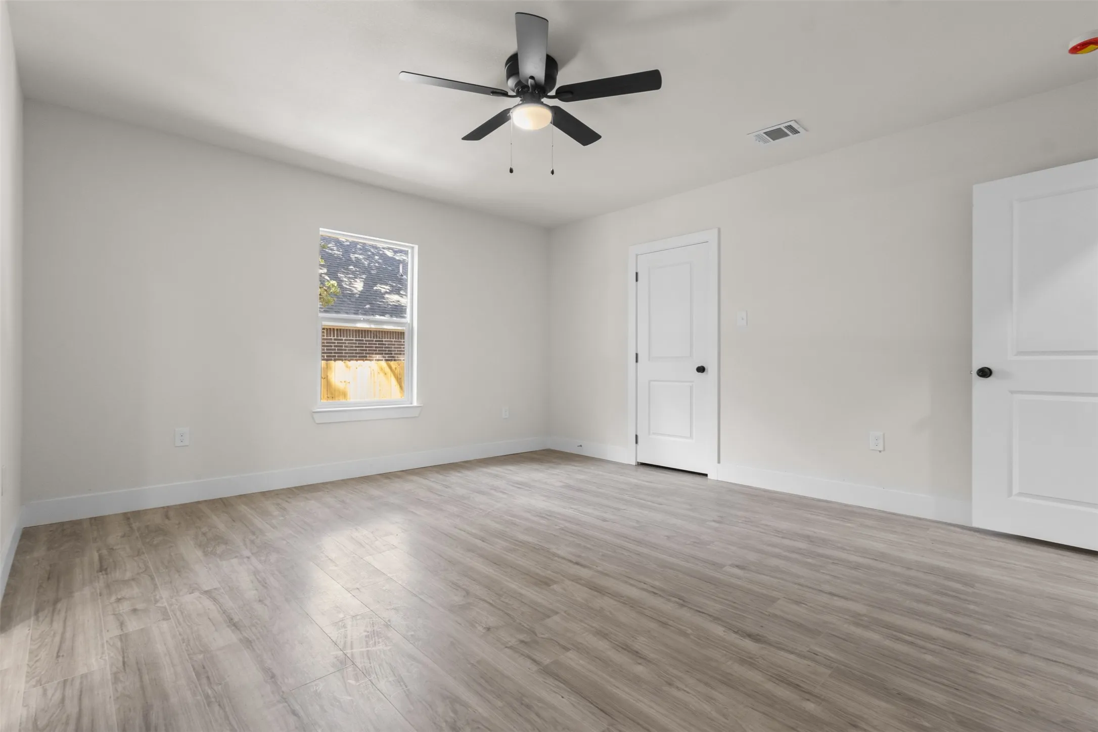 Wood-finish flooring, white walls, black ceiling fan with integrated lighting, and two panel doors