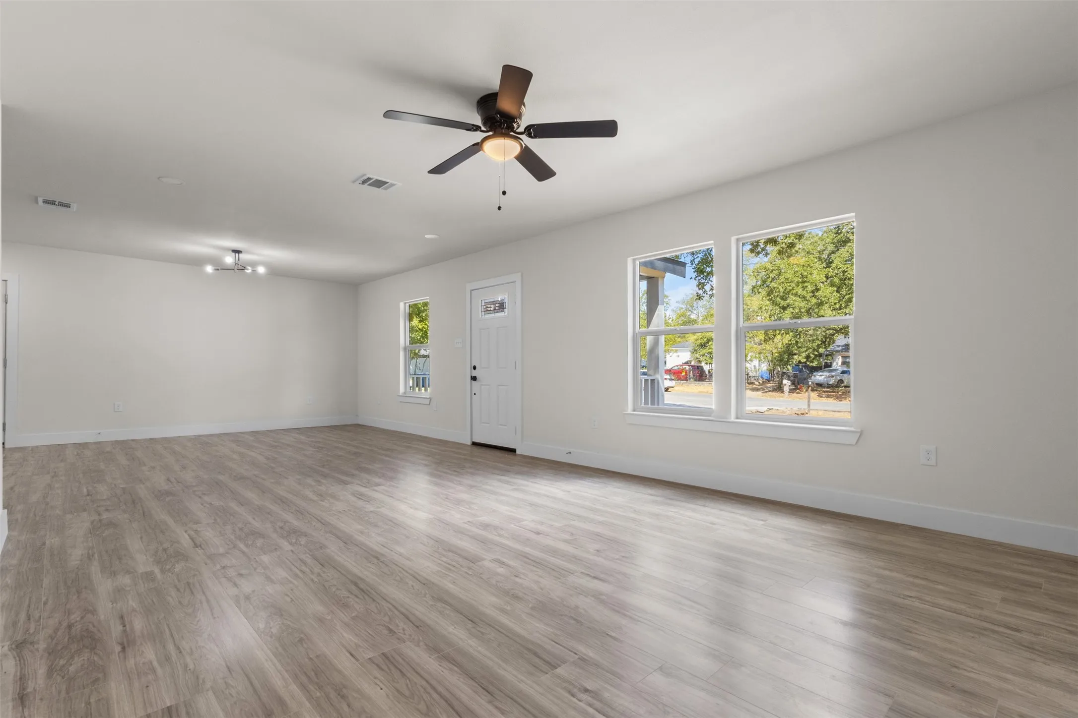 Expansive interior with wood-finish flooring, multiple windows, and a ceiling fan