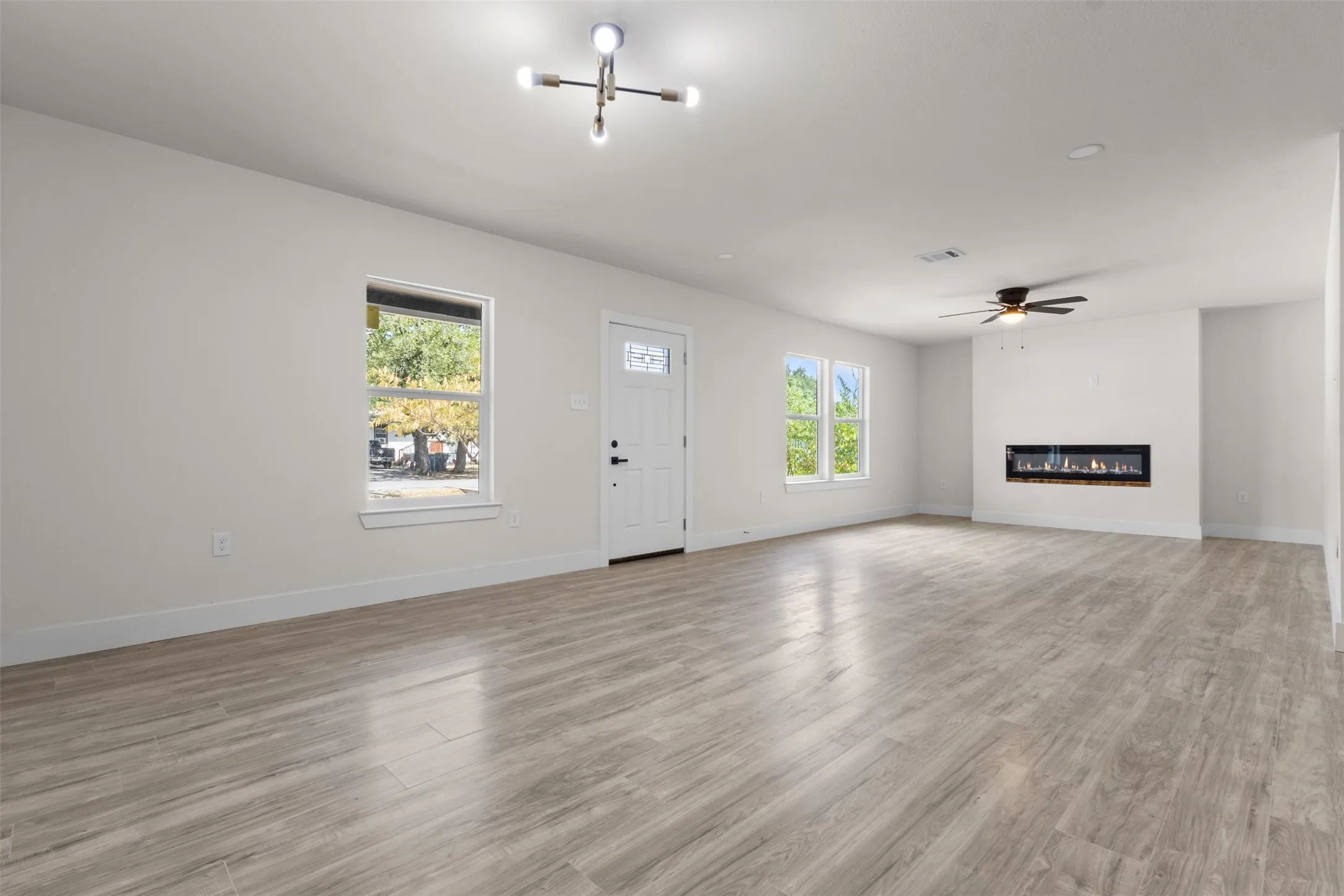 Spacious living area with wood-finish flooring, multiple windows, a modern linear electric fireplace, and a ceiling fan