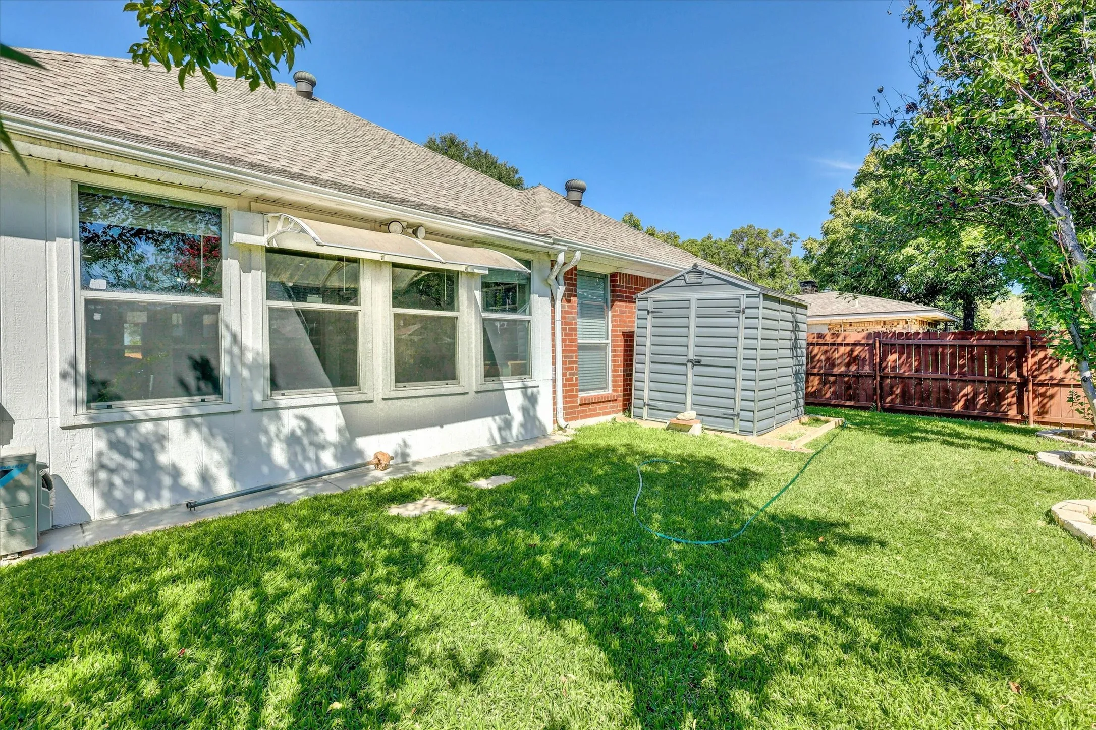 Expansive grassy yard with mature trees, a durable storage shed, and privacy fencing