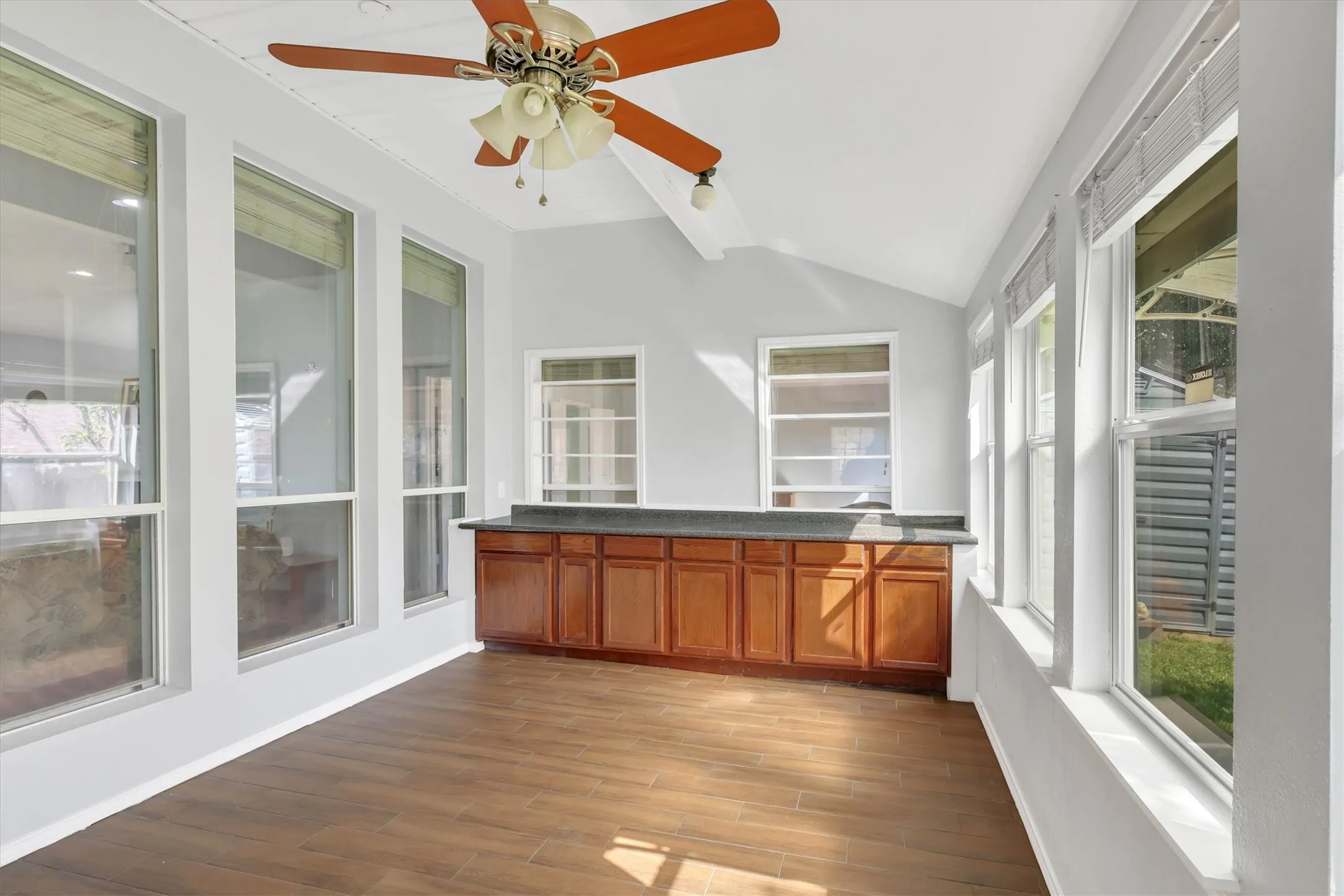 Vaulted ceiling with a ceiling fan, extensive windows, wood-finish flooring, and built-in cabinetry with a countertop