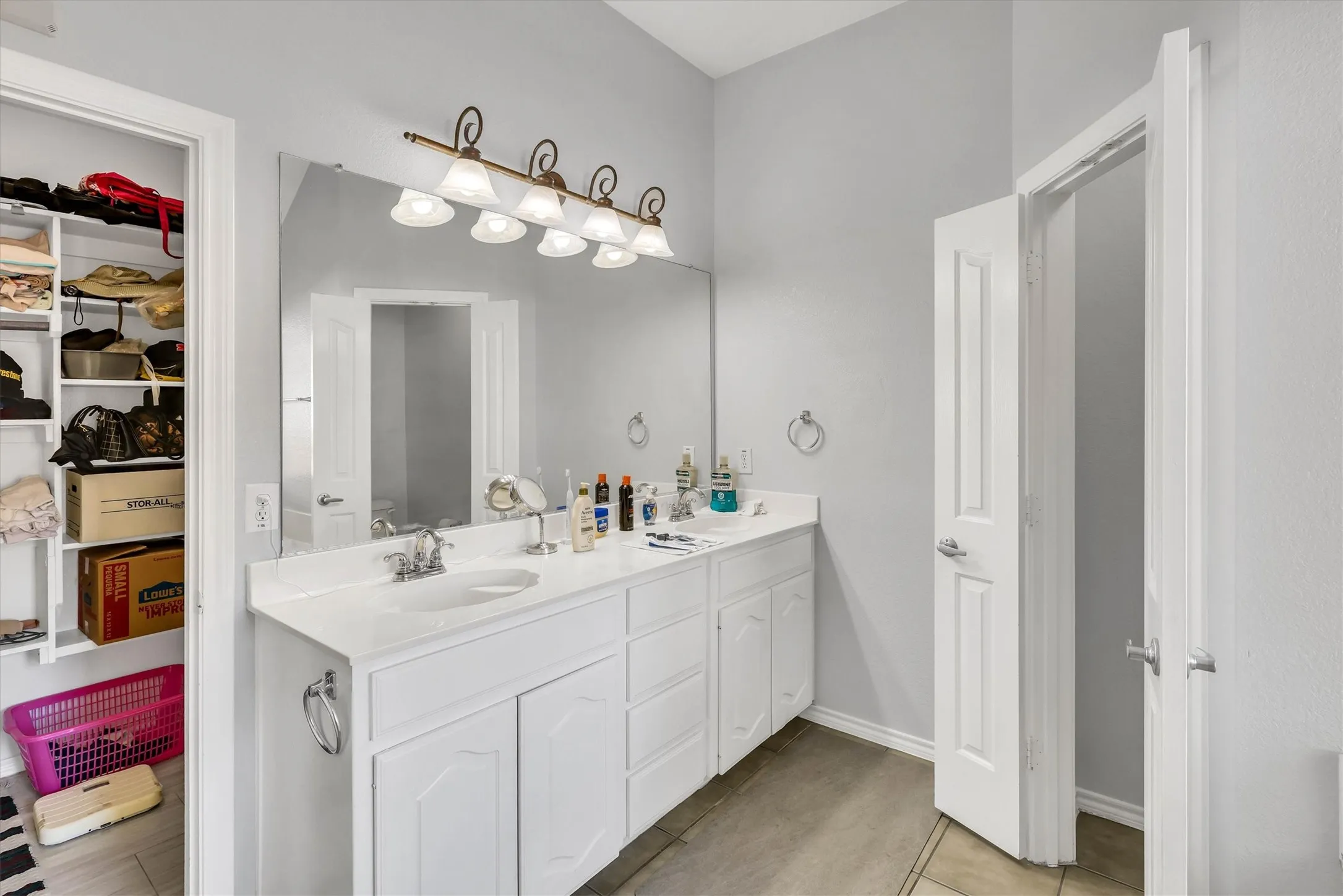 Dual-sink vanity with white cabinetry and integrated countertop, large vanity mirror, and overhead lighting fixture