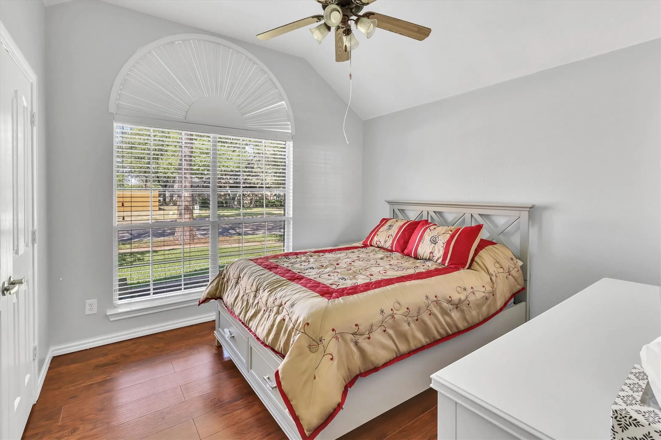 Vaulted ceiling, arched window with blinds, wood-finish flooring, and a ceiling fan