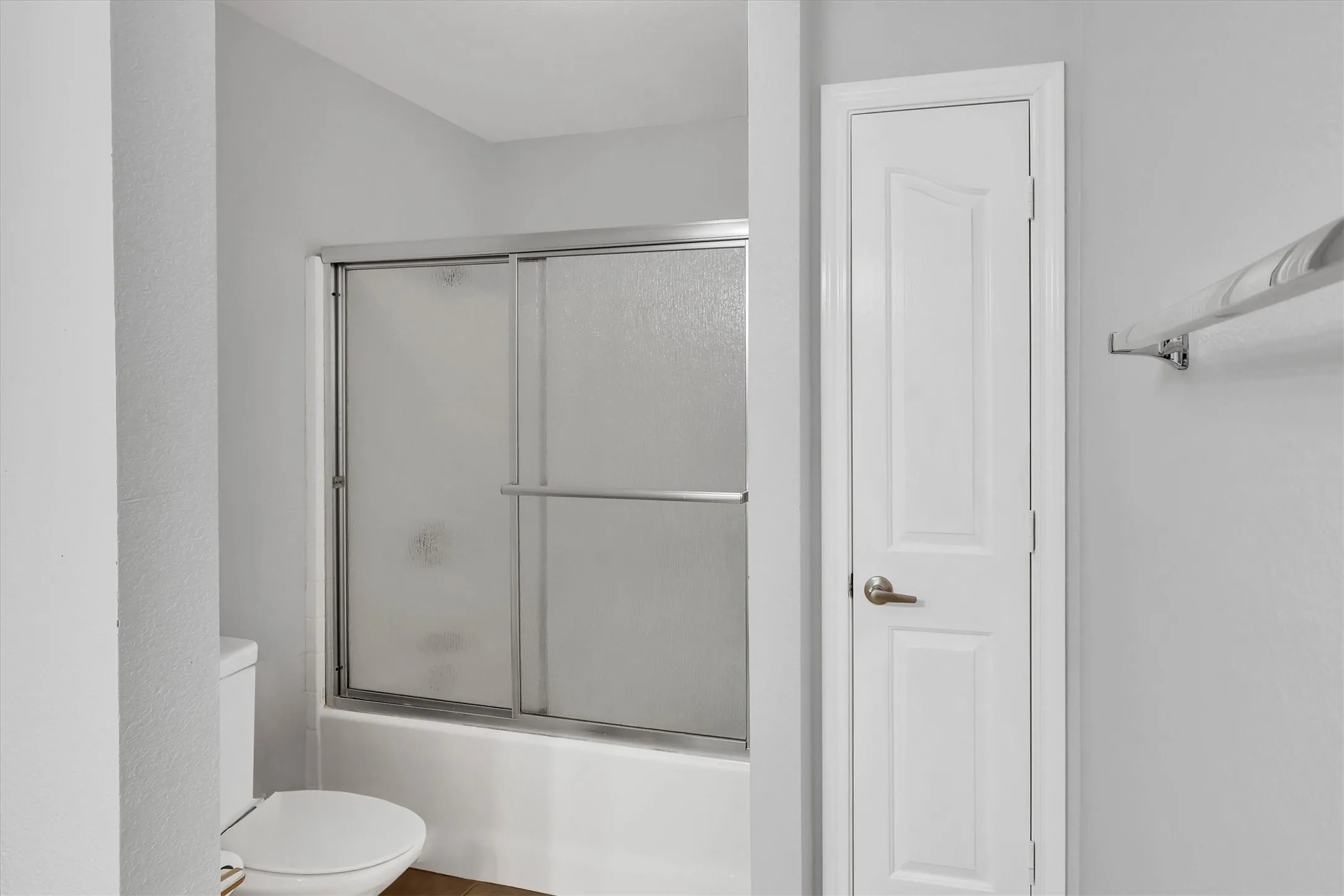 White bathtub with sliding glass doors, adjacent to a white toilet, and a paneled interior door