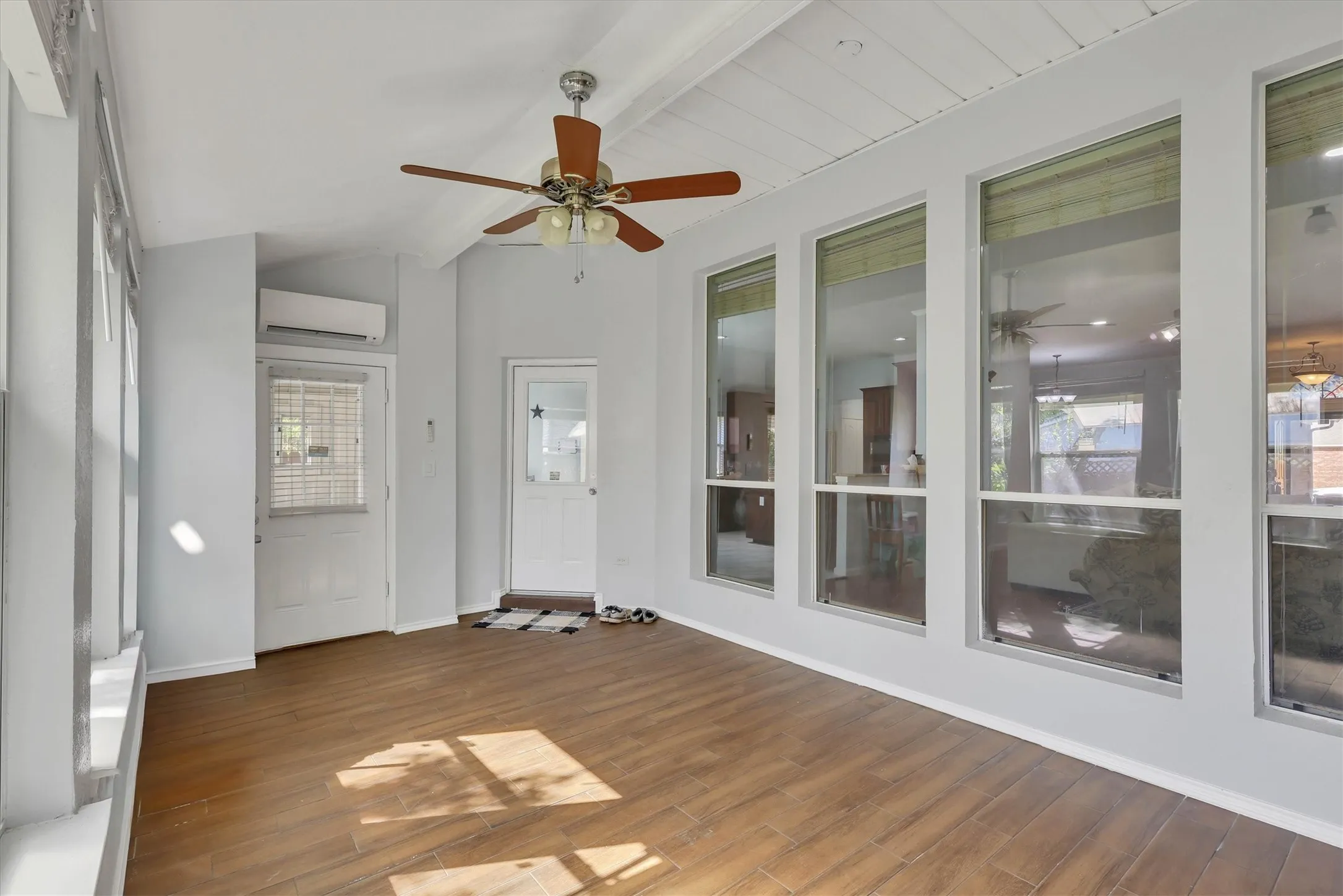 Wood-finish flooring with multiple windows, two exterior doors, a ceiling fan, and a wall-mounted mini-split unit