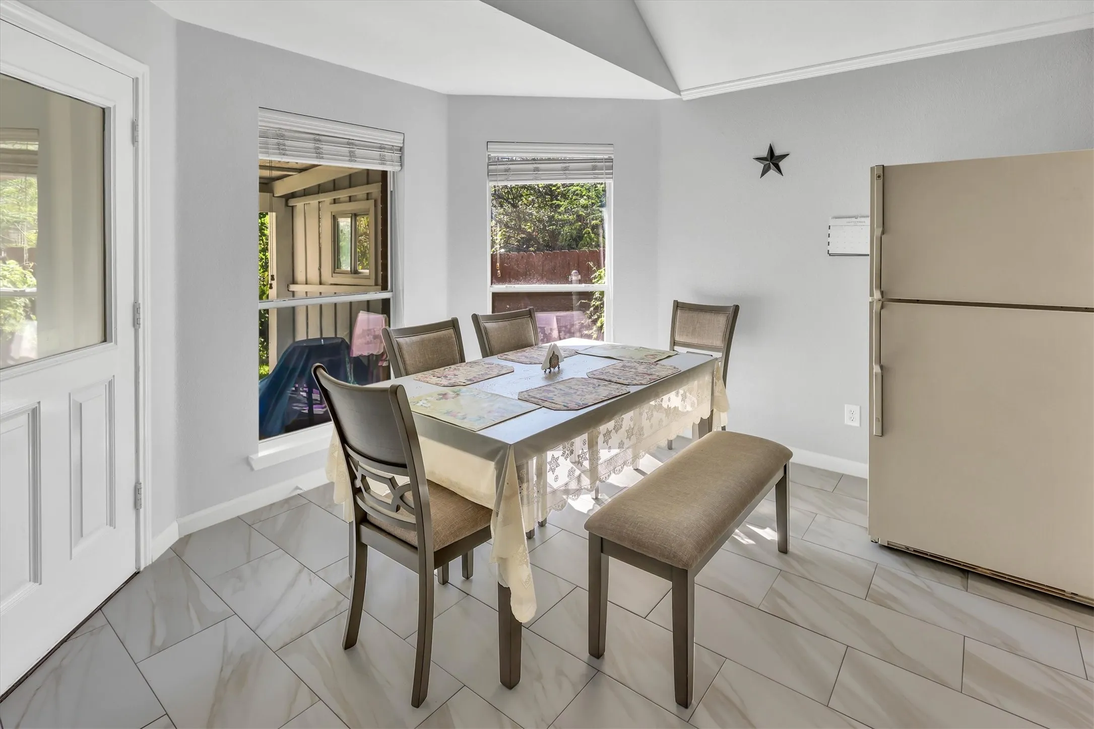 Light-toned wall paint with a vaulted ceiling, bay windows, and tiled flooring