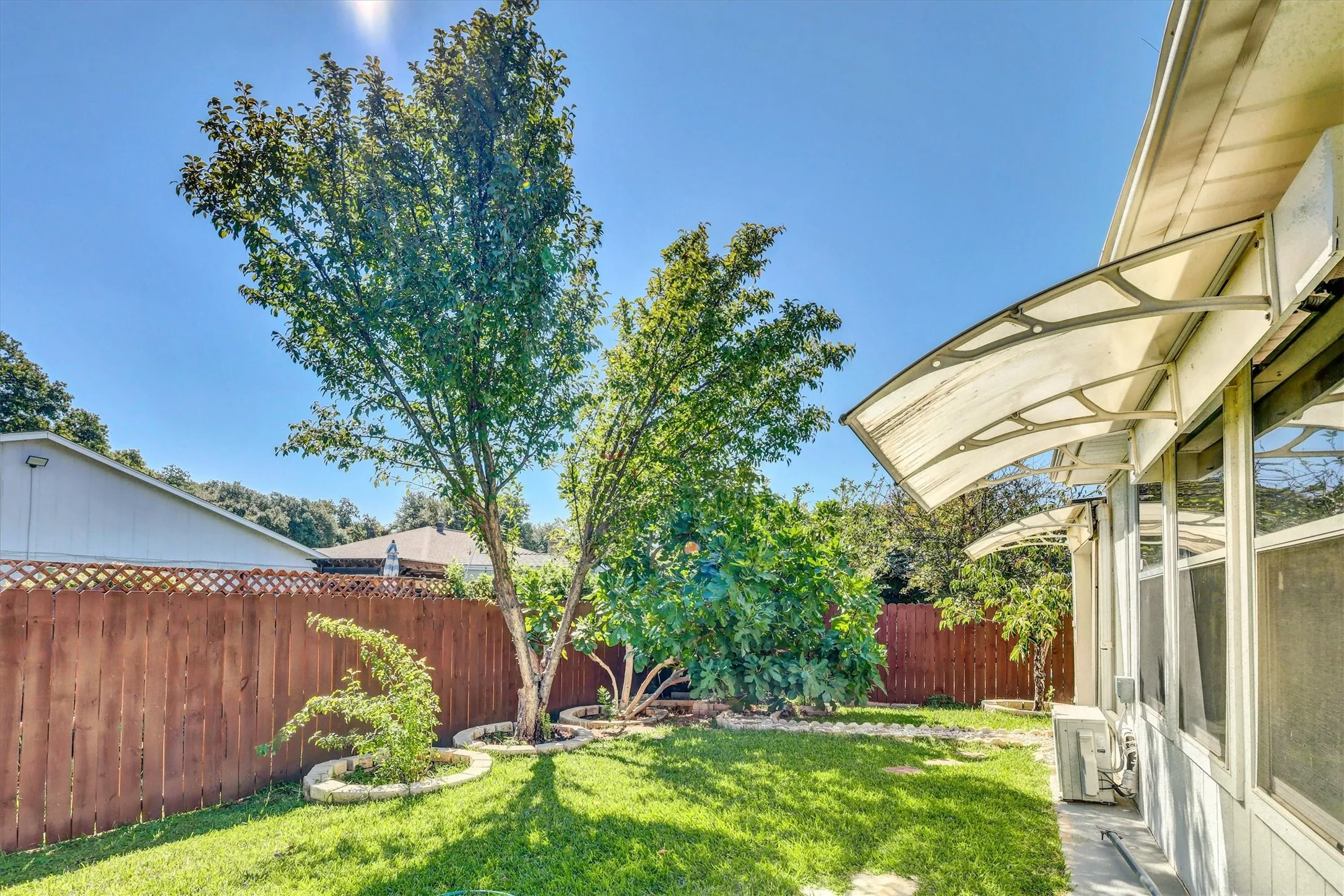 Fenced backyard featuring a manicured lawn, established trees, and perimeter landscaping