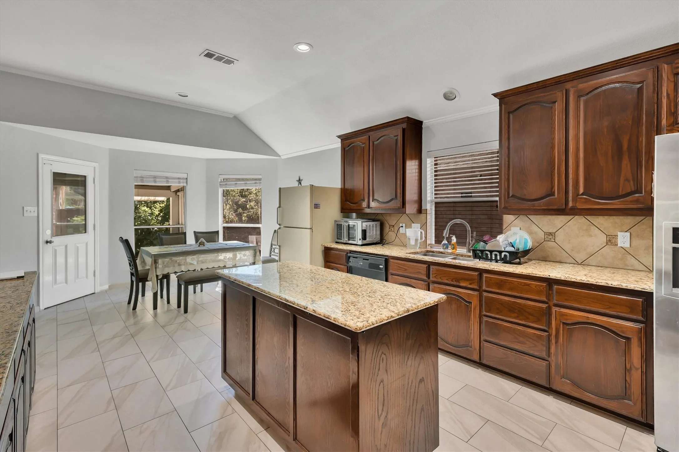 Central kitchen island with granite countertop, wood cabinetry, tile flooring, and integrated dining area with bay windows